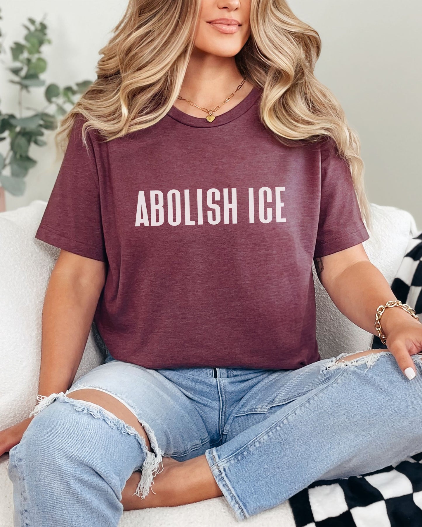 Person wearing a maroon t-shirt with 'ABOLISH ICE' text, sitting on a couch.