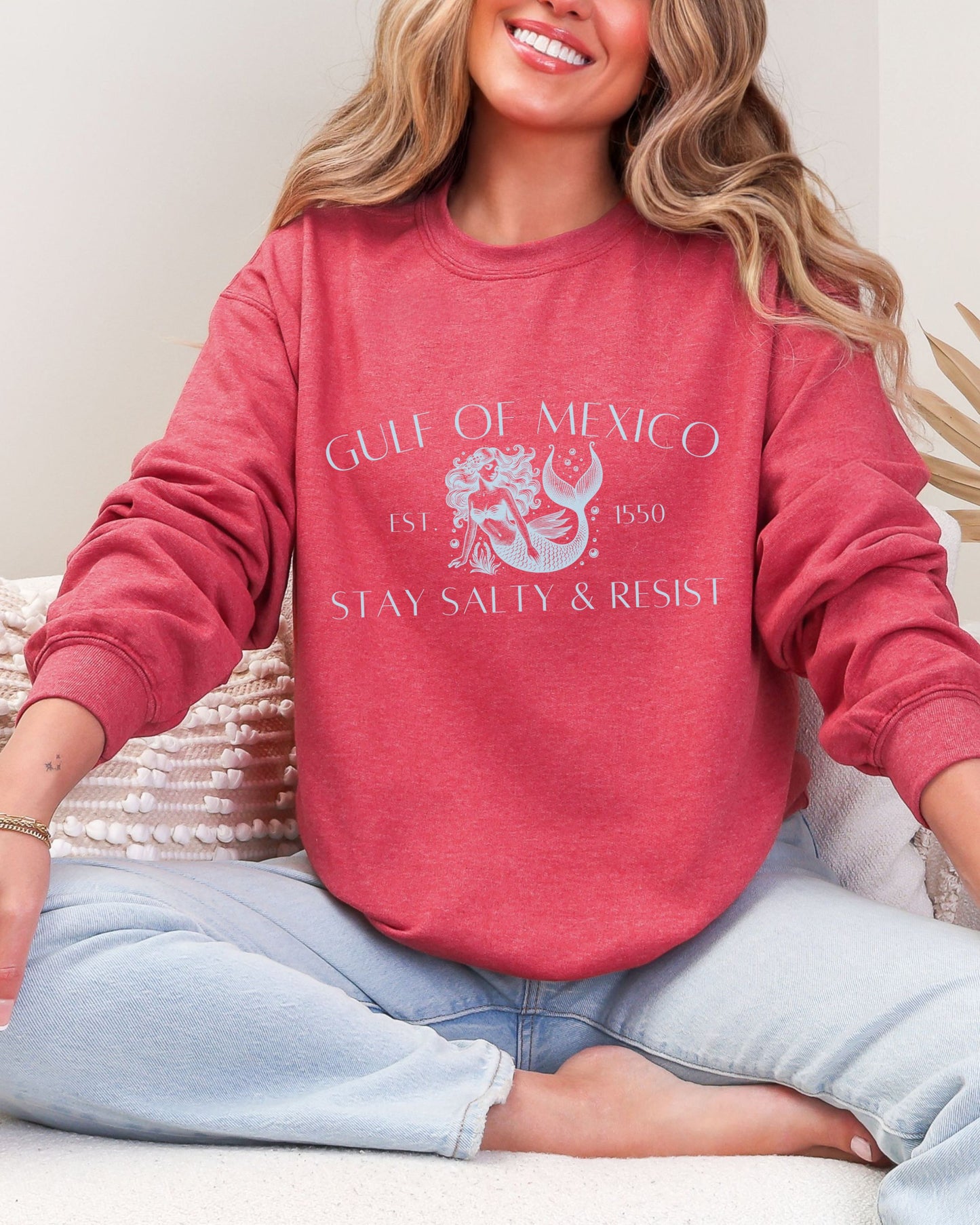 Person wearing a red sweatshirt with text and graphics, sitting on a white surface.