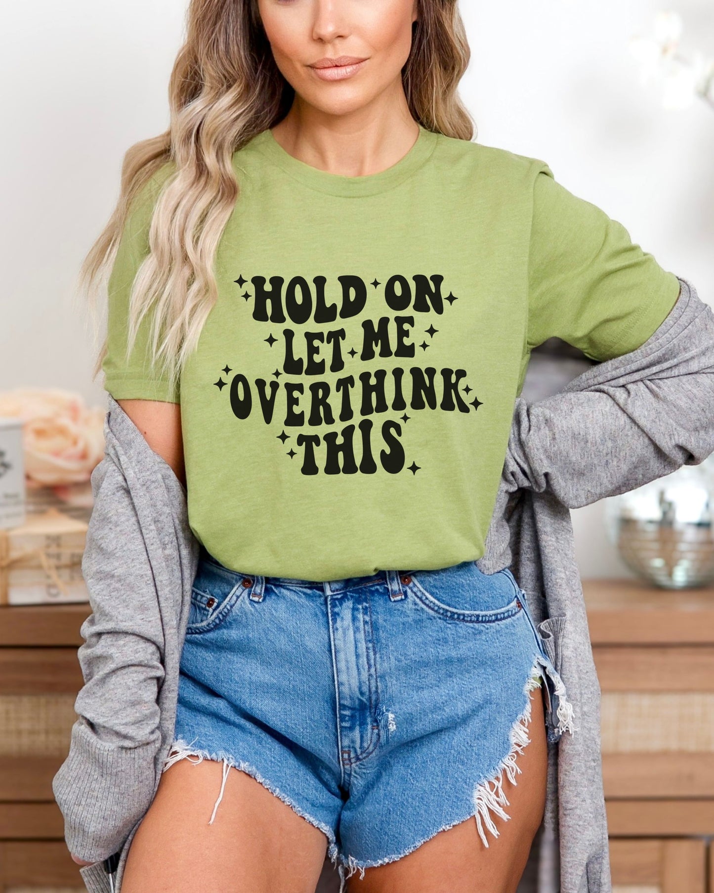 Person wearing a green tshirt with text and denim shorts indoors.