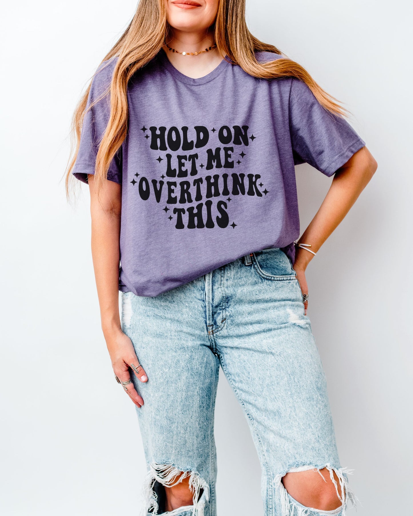 Person wearing a purple t-shirt with text and ripped jeans on a plain background