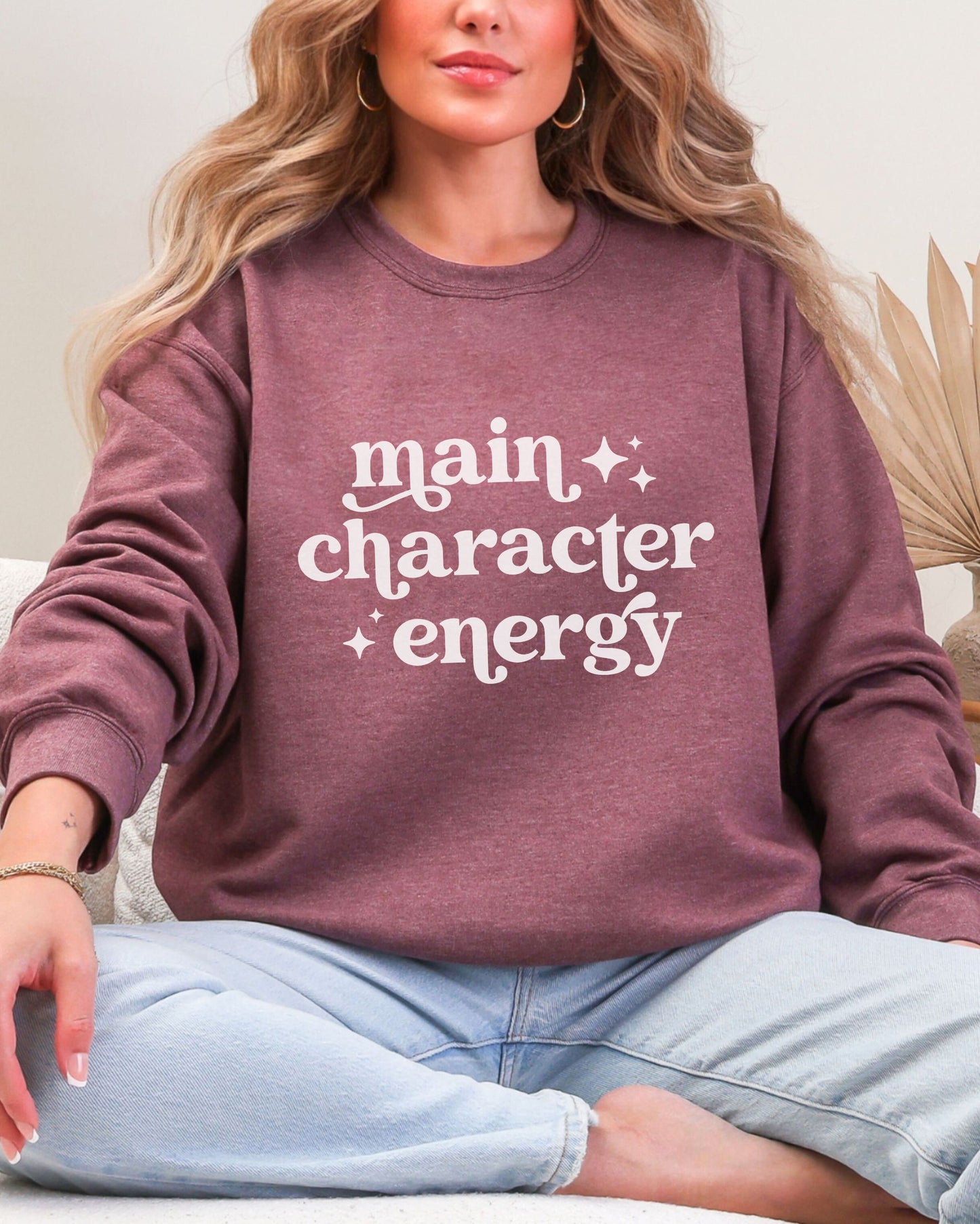 Person wearing a maroon sweatshirt with 'main character energy' text.