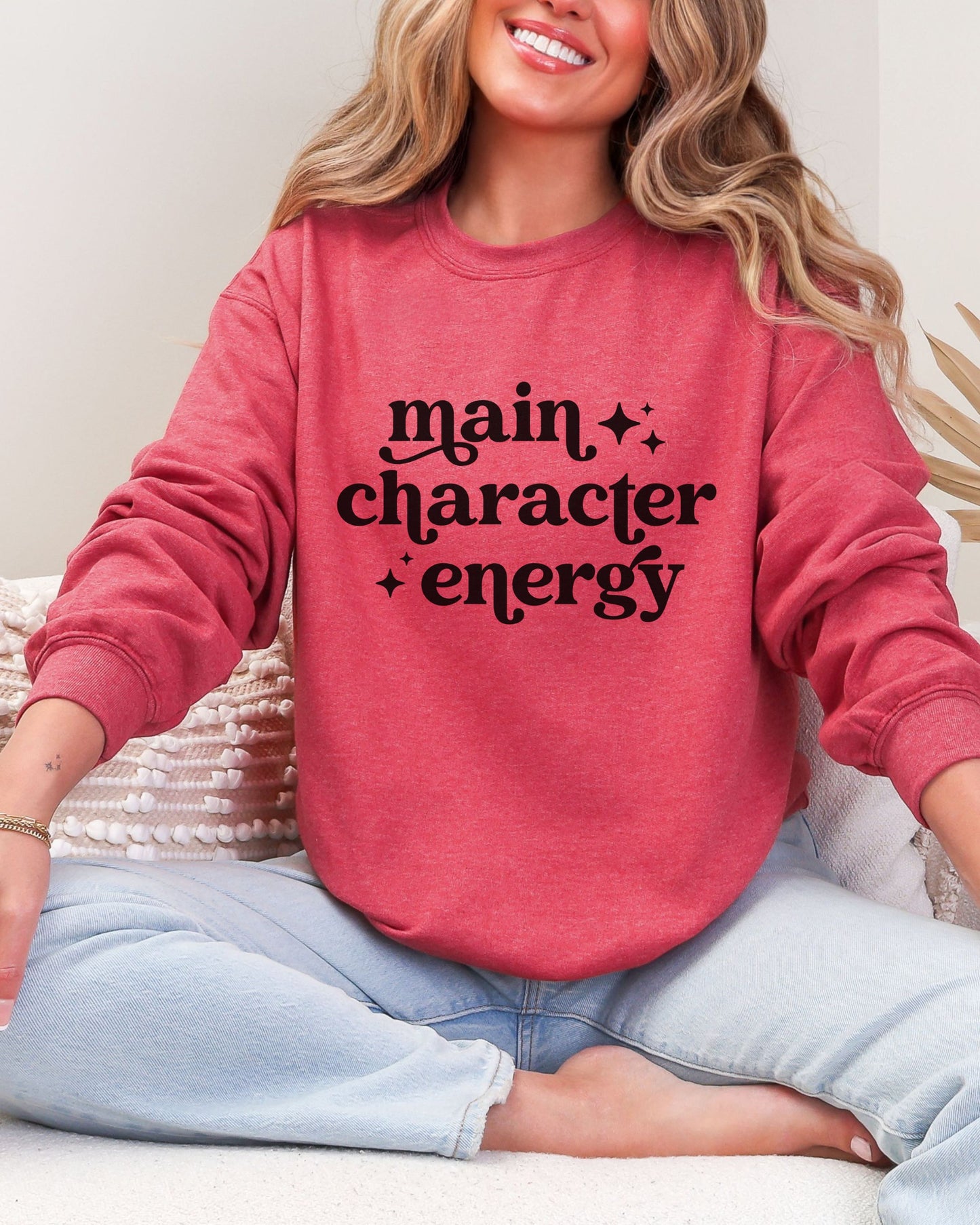 Person wearing a red sweatshirt with 'main character energy' text, sitting on a white surface.