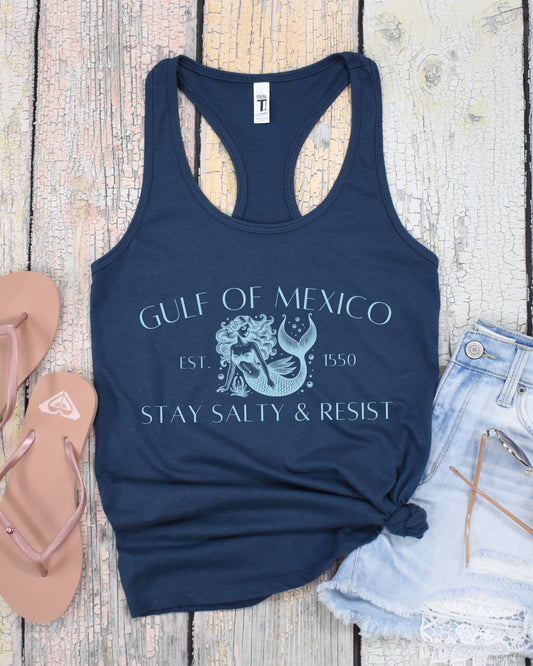 Navy blue tank top with graphic design and text on a wooden surface with sandals and denim shorts.