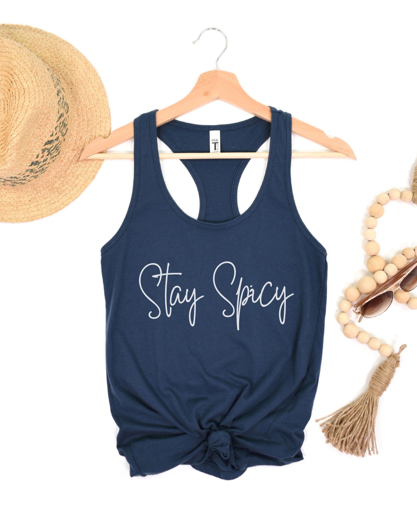Navy blue tank top with 'Stay Spicy' text on a hanger with decorative items.