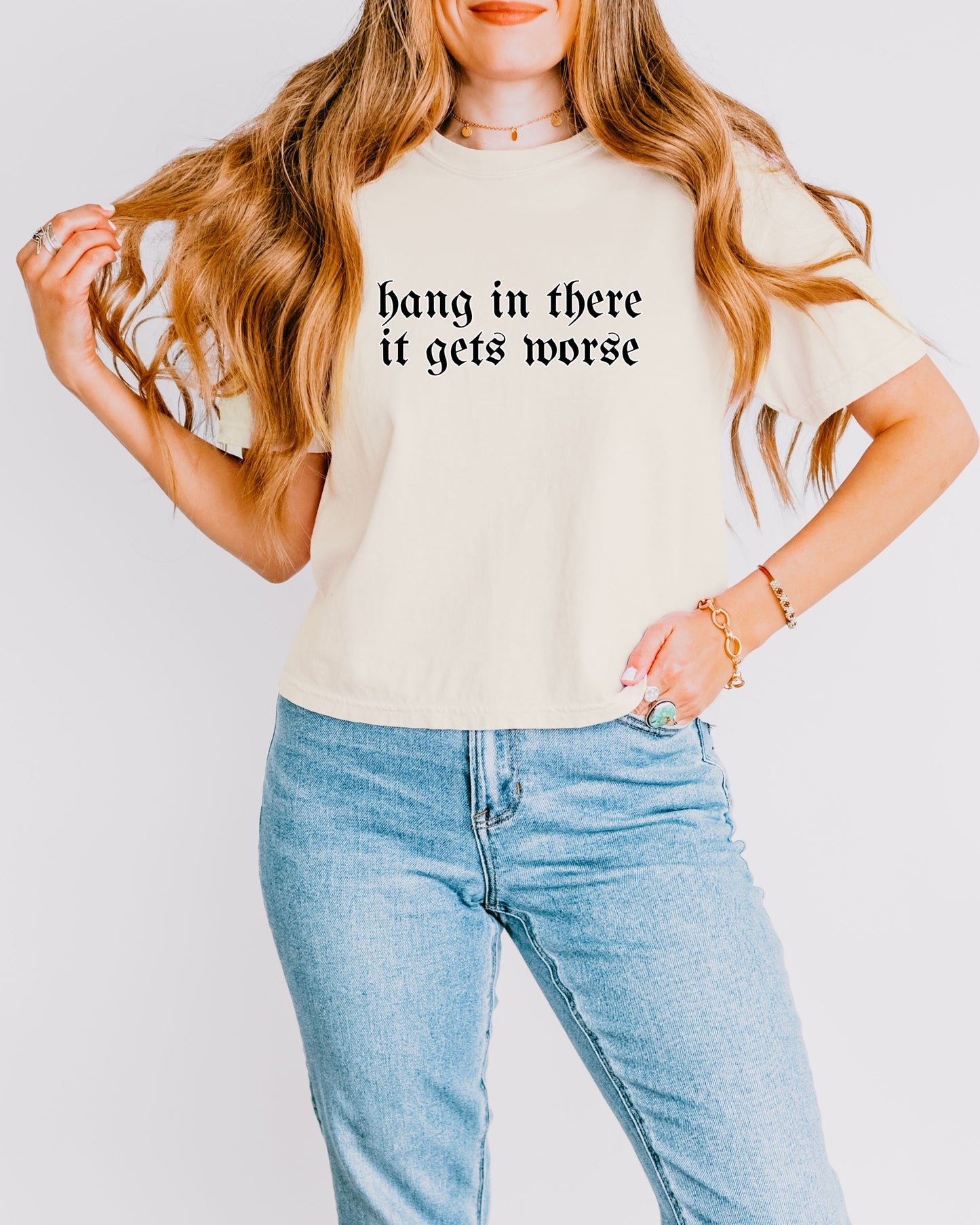 Person wearing a beige t-shirt with text and blue jeans on a plain background