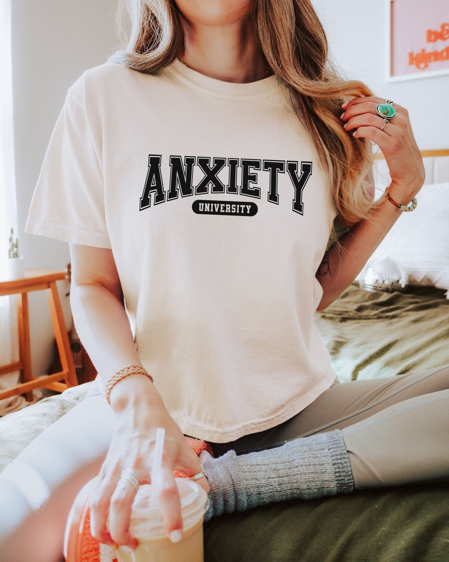 Person wearing an ivory t-shirt with 'ANXIETY UNIVERSITY' text.