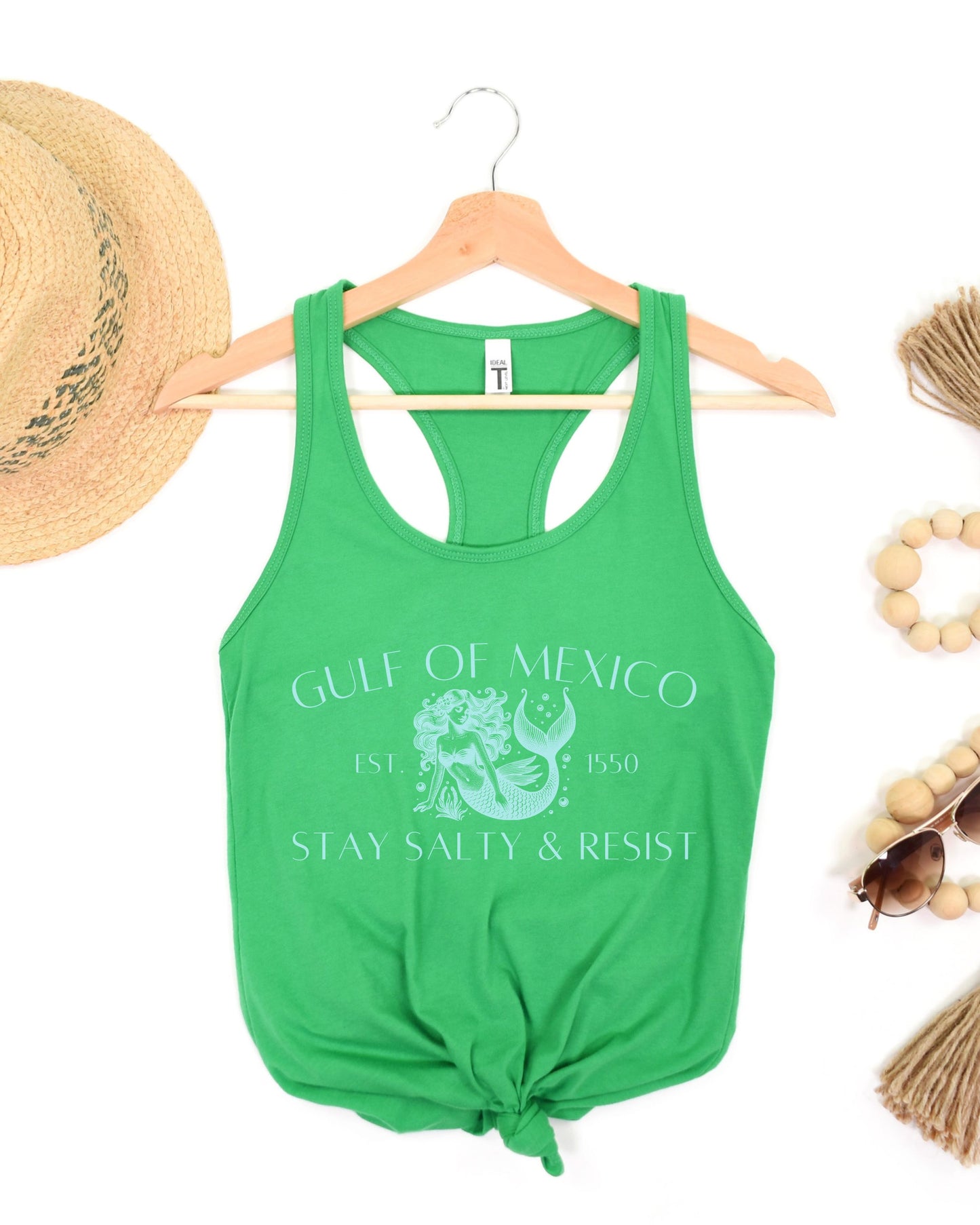 Green tank top with 'Gulf of Mexico' text on a hanger with accessories around.