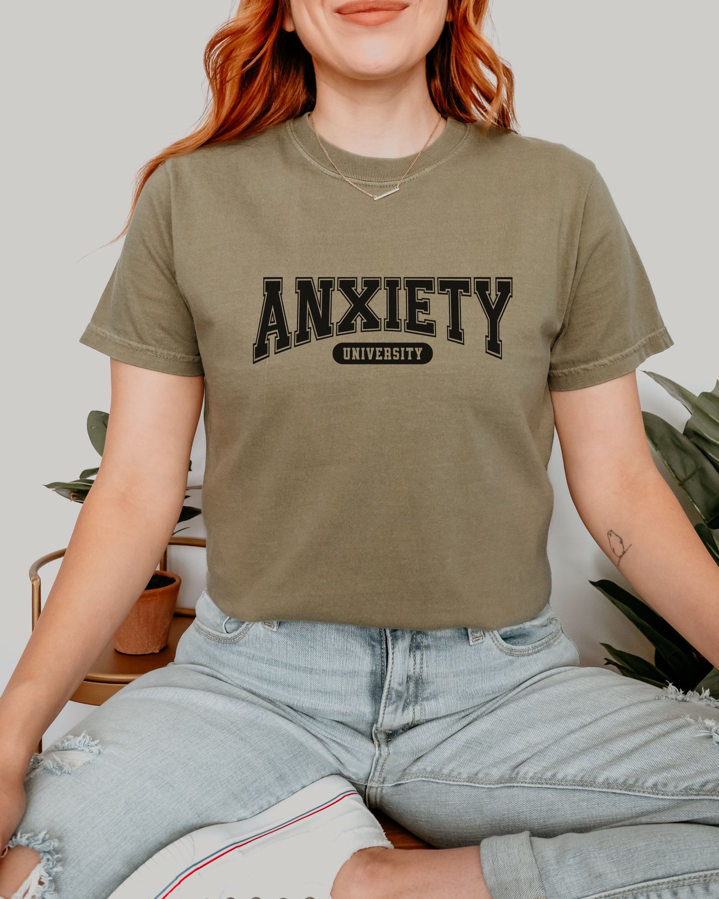 Person wearing a khaki t-shirt with 'ANXIETY UNIVERSITY' text.