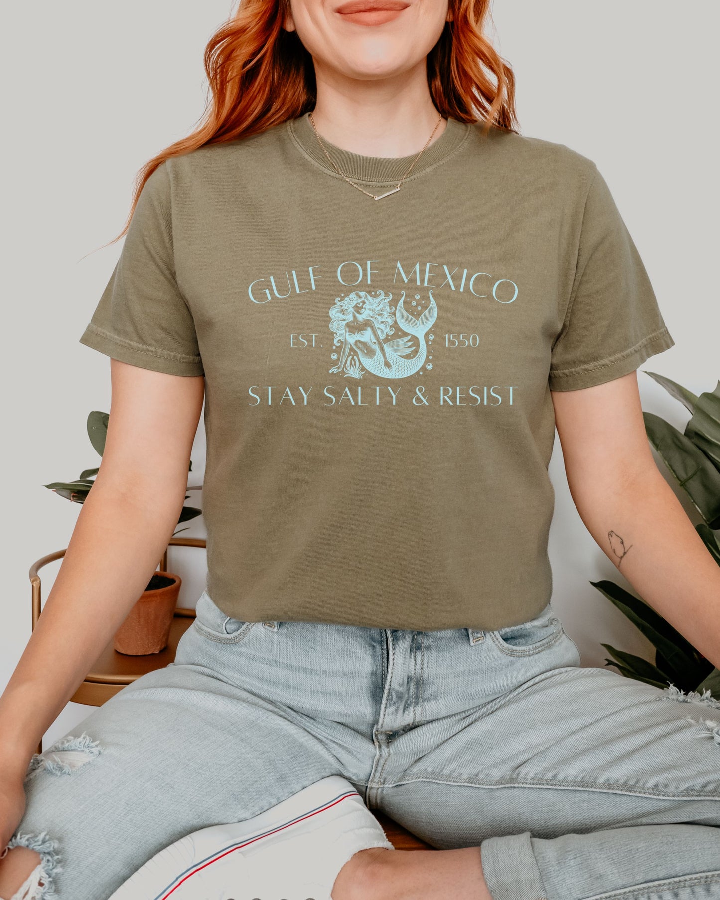 Person wearing a green t-shirt with 'Gulf of Mexico' text and graphic, sitting indoors.