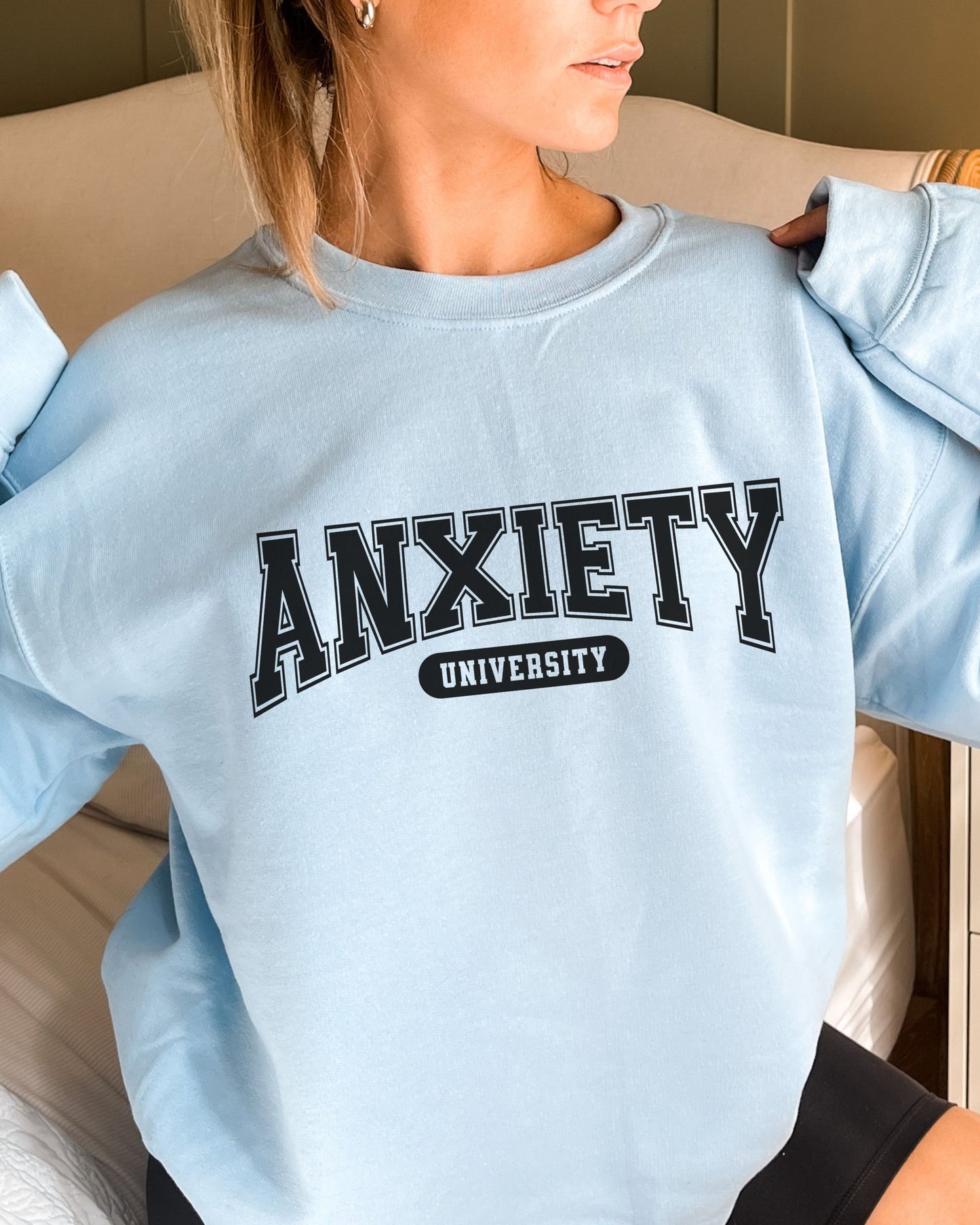 Light blue sweatshirt with 'ANXIETY UNIVERSITY' text worn by a person.