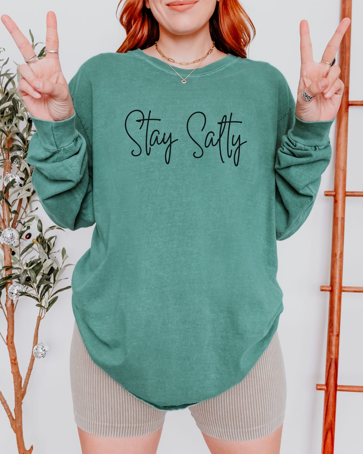 Person wearing a green sweatshirt with 'Stay Salty' text, making peace signs.