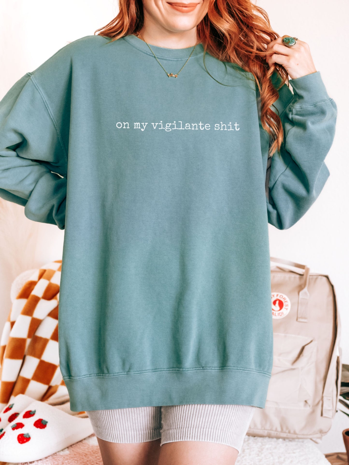 Person wearing a teal sweatshirt with text, standing in a casual indoor setting.