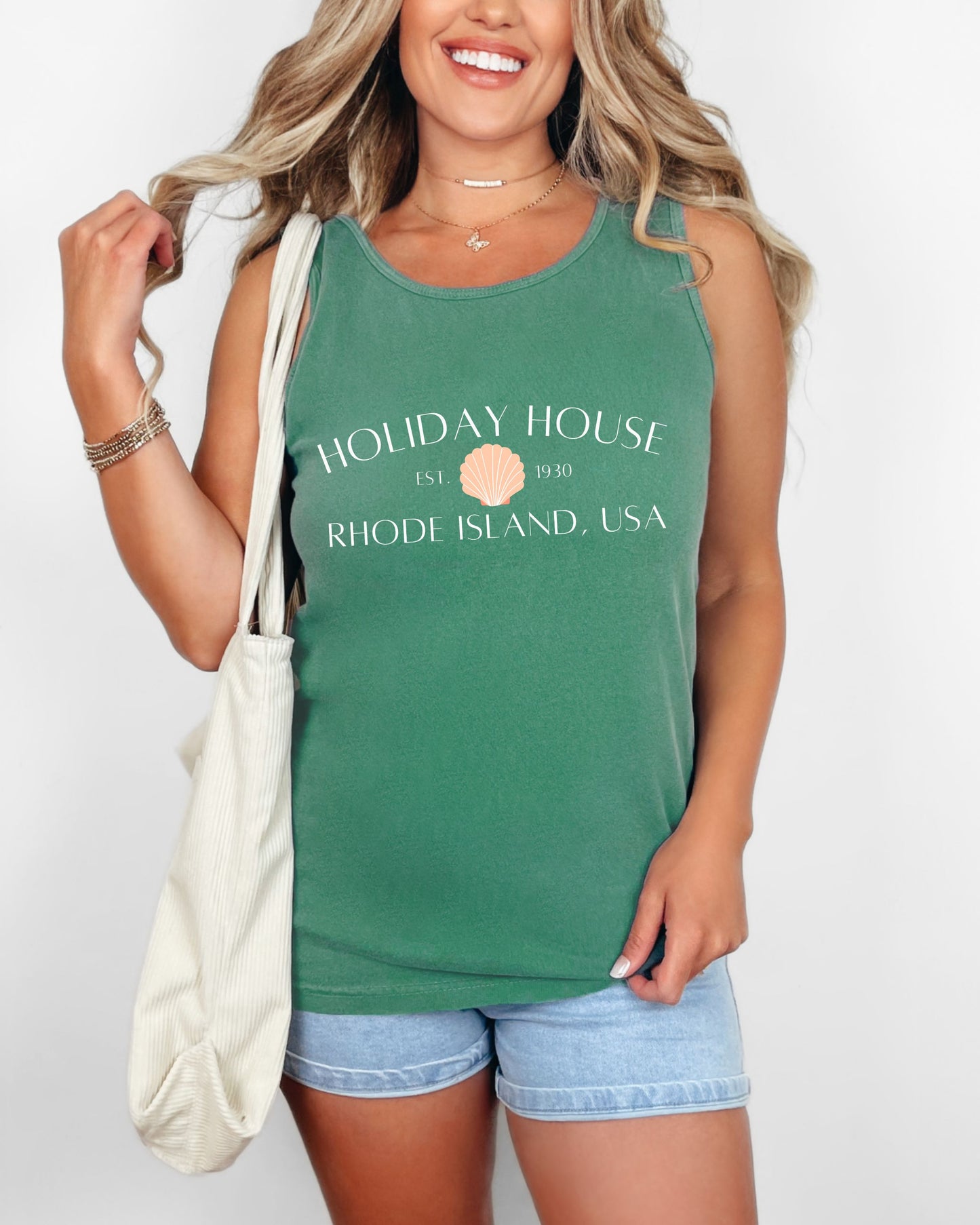 Woman wearing a green tank top with 'Holiday House' text, holding a white bag on a plain background