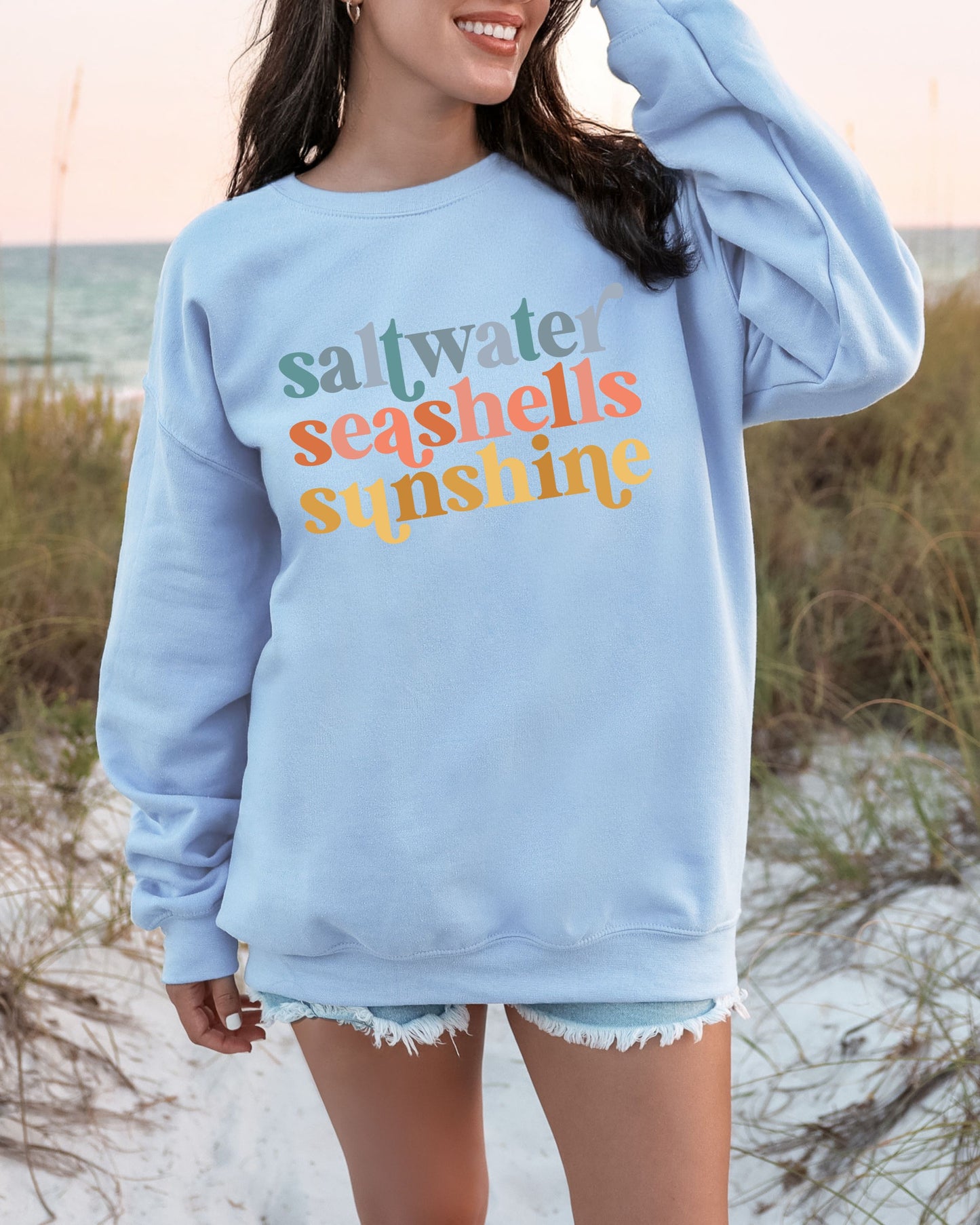 Person wearing a light blue sweatshirt with colorful text on a beach.