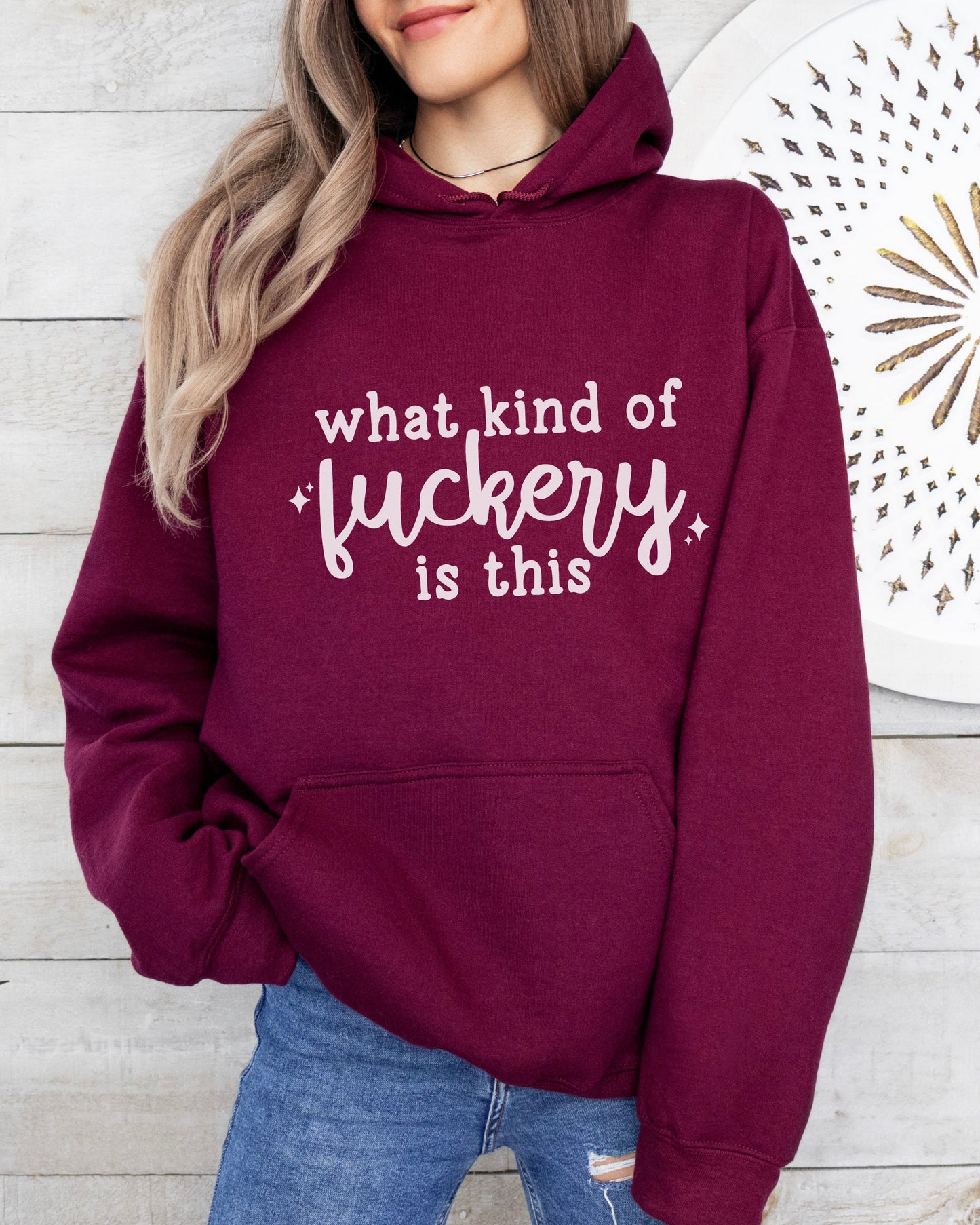 Person wearing a maroon hoodie with text in white, standing against a wooden wall.