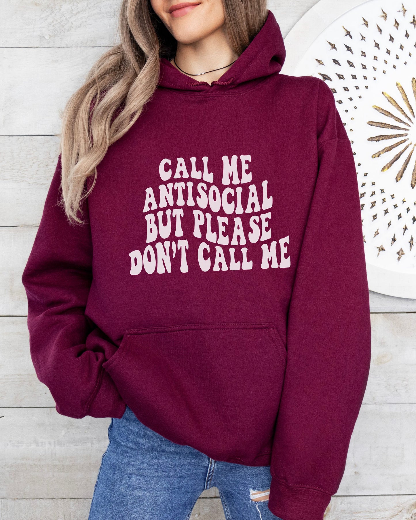 Person wearing a maroon hoodie with text, standing against a wooden wall.