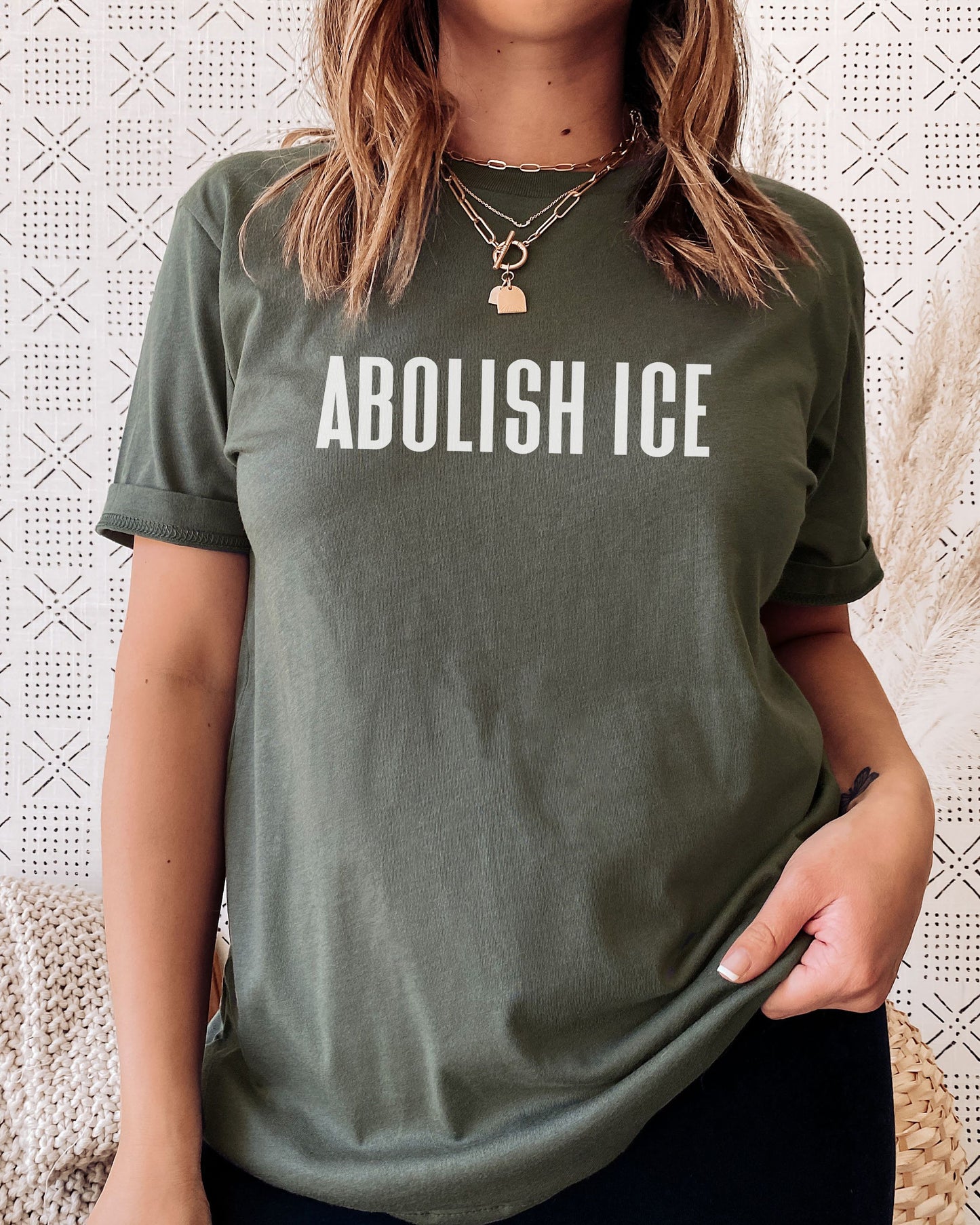 Person wearing a green t-shirt with 'ABOLISH ICE' text against a textured white background