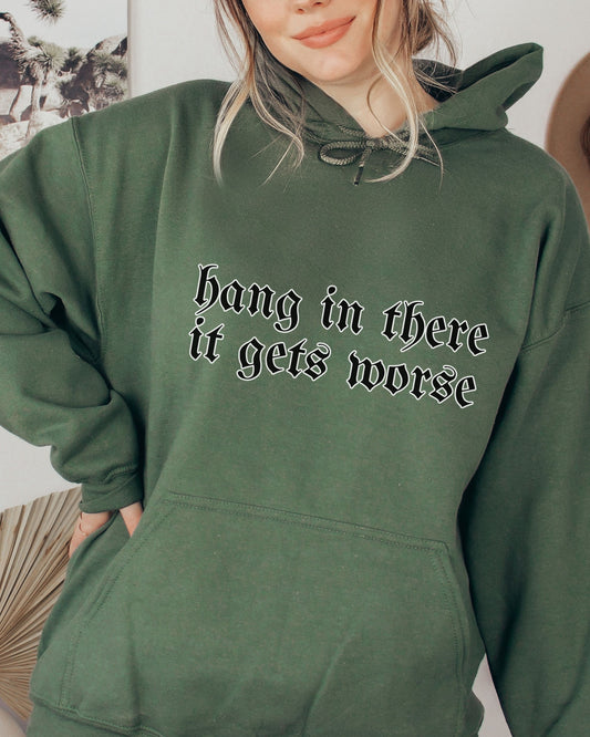 Person wearing a green hoodie with text 'hang in there it gets worse' on a neutral background