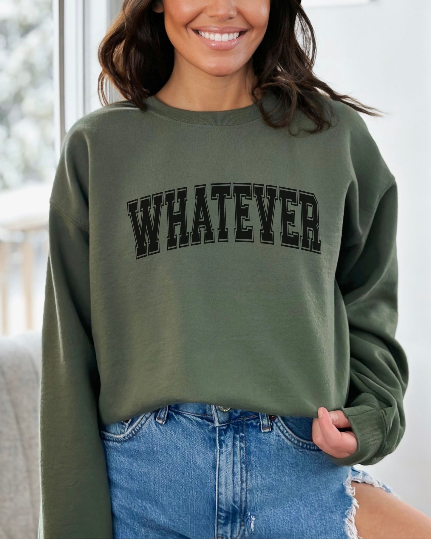 Person wearing a green sweatshirt with 'WHATEVER' text, standing indoors.