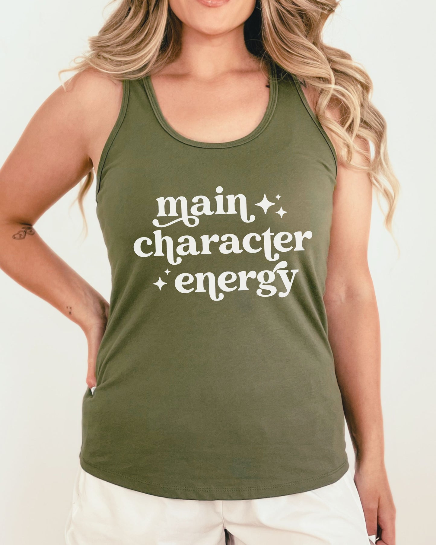Person wearing a green tank top with 'main character energy' text on a plain background