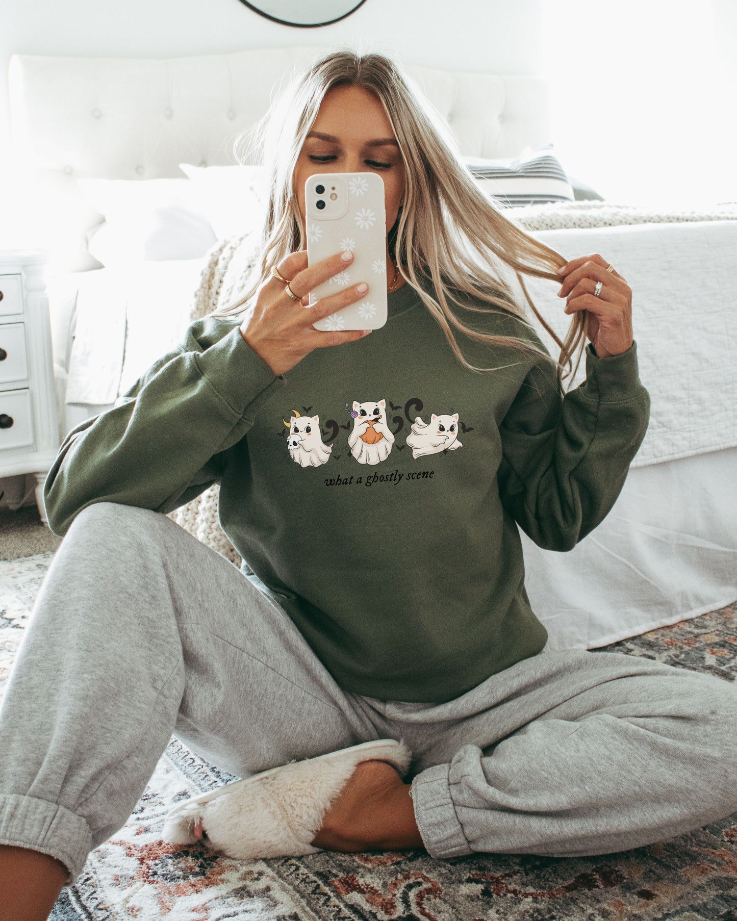 Person wearing a green sweatshirt with cat illustrations and gray pants sitting on a bed.