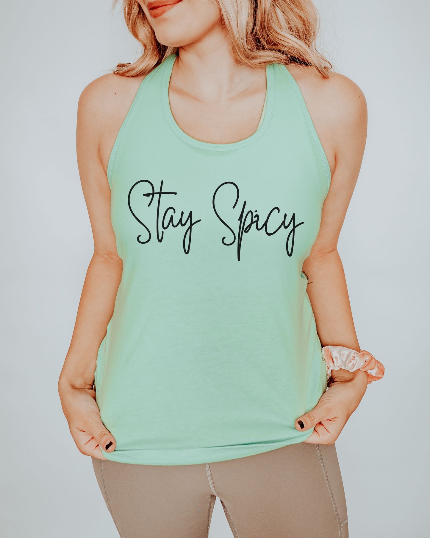 Person wearing a mint green tank top with 'Stay Spicy' text on a plain background