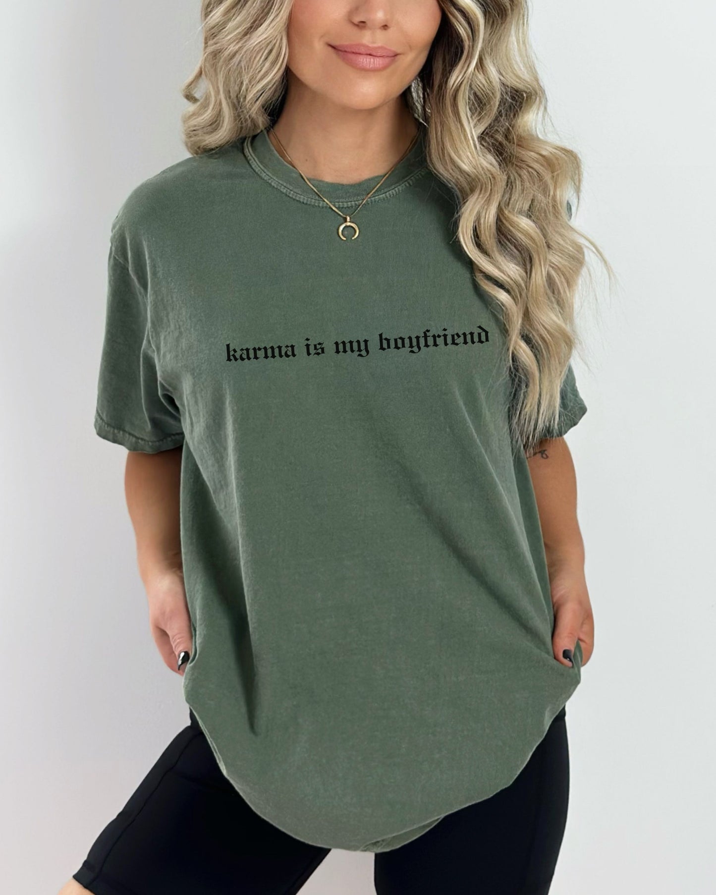 Person wearing a green t-shirt with 'karma is my boyfriend' text on a plain background