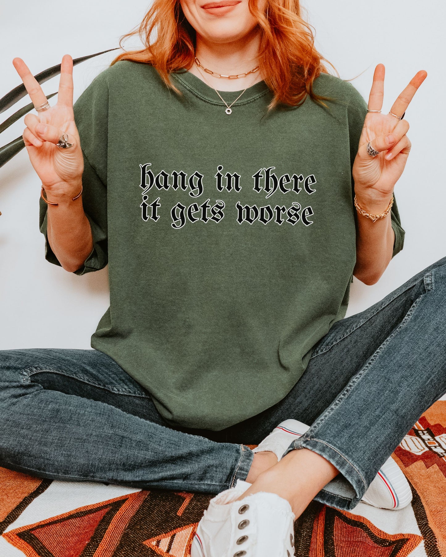 Person wearing a green sweatshirt with text, sitting on a patterned rug.