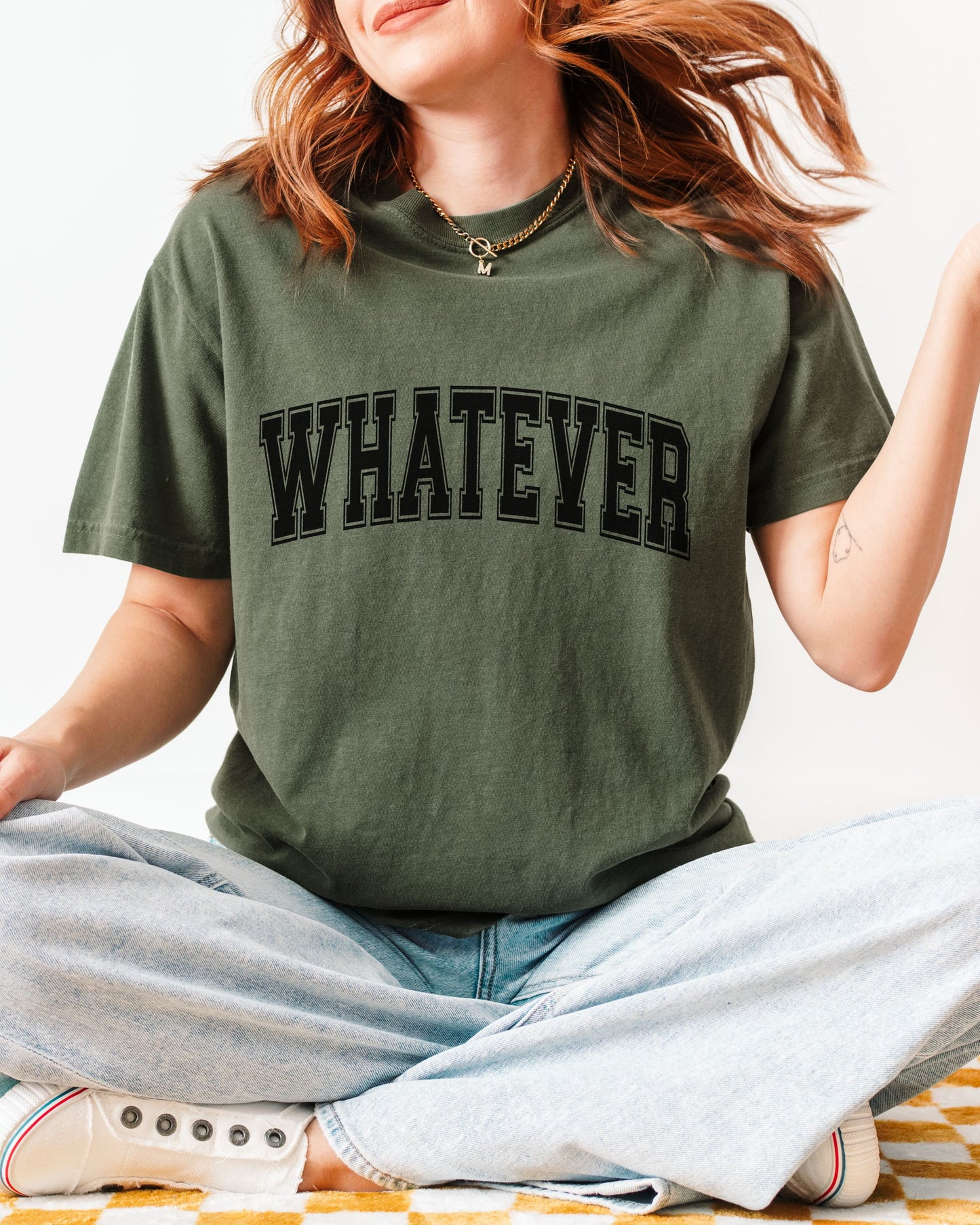 Person wearing a green t-shirt with 'WHATEVER' text, sitting on a striped surface.
