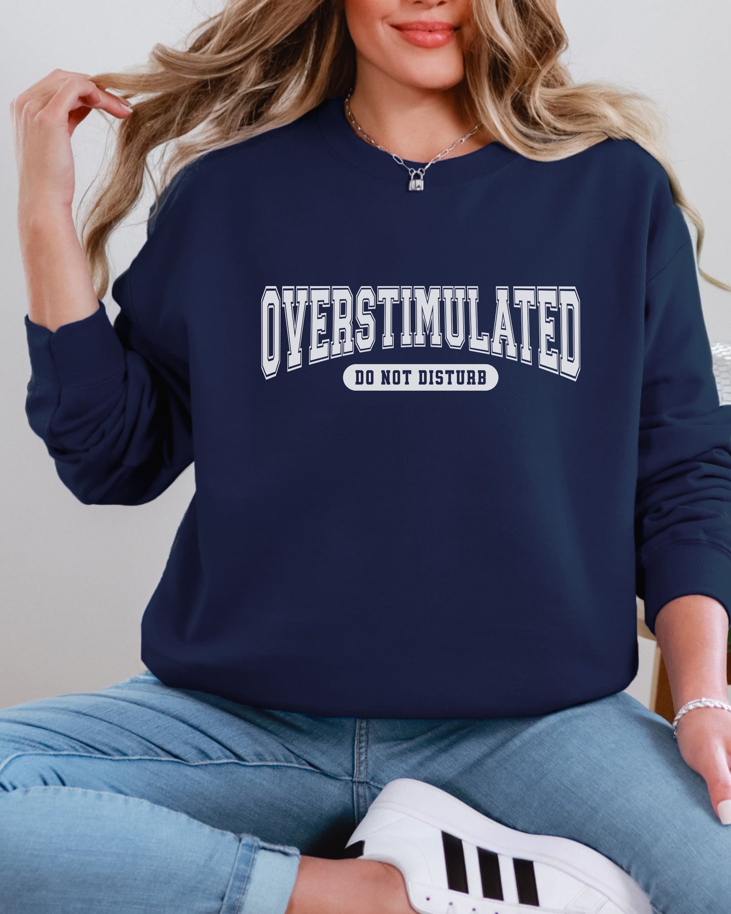 Person wearing a navy sweatshirt with 'OVERSTIMULATED DO NOT DISTURB' text, sitting on a light-colored surface.