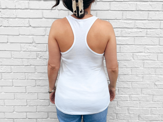 Person wearing a white tank top and blue jeans against a white brick wall.