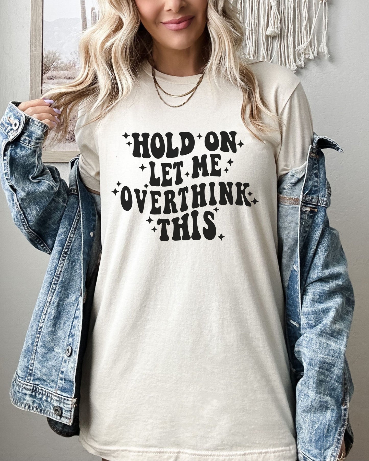 Person wearing an ivory tshirt with text 'Hold on let me overthink this' and a denim jacket.