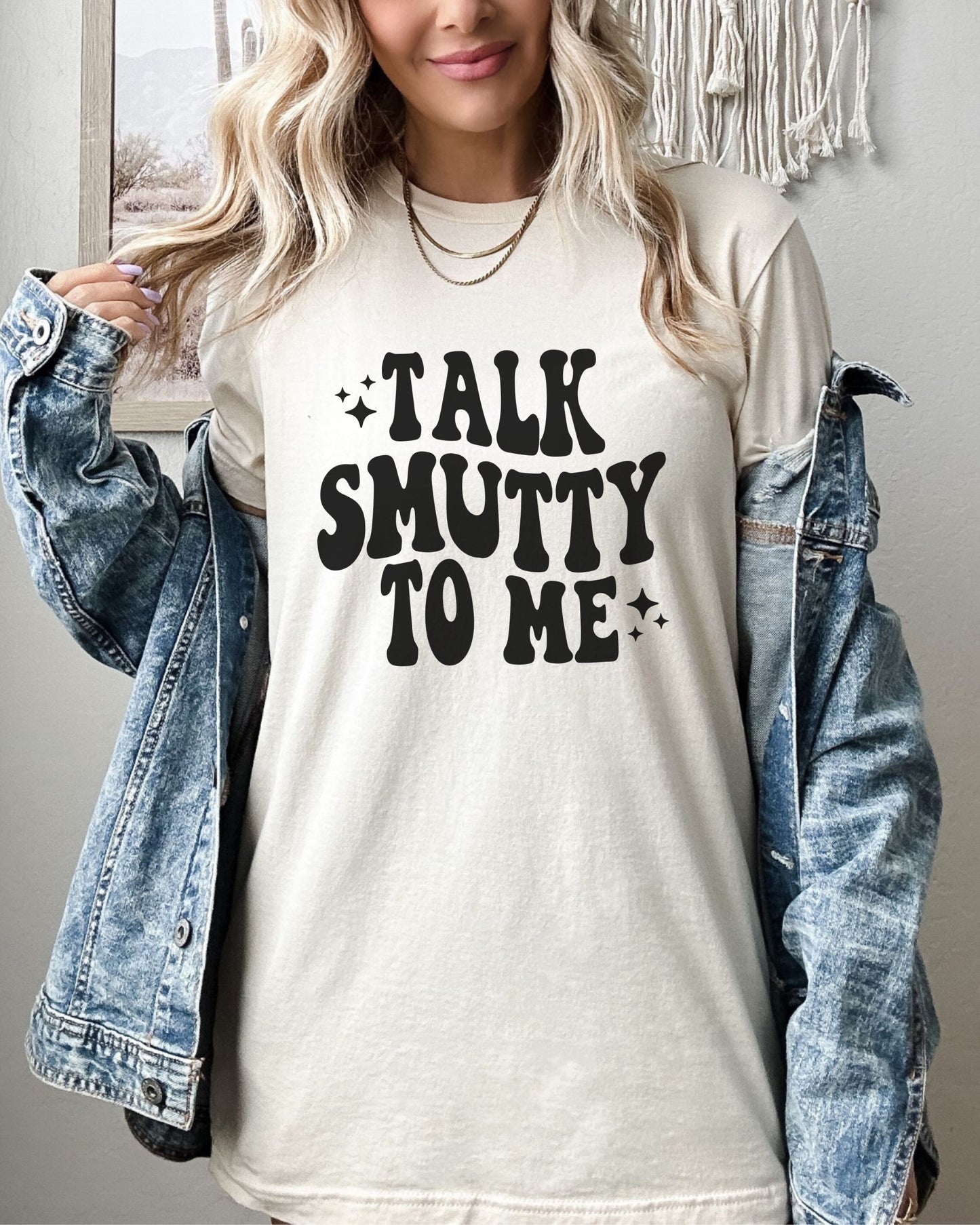 Person wearing a white t-shirt with 'Talk Smutty To Me' text, paired with a denim jacket.