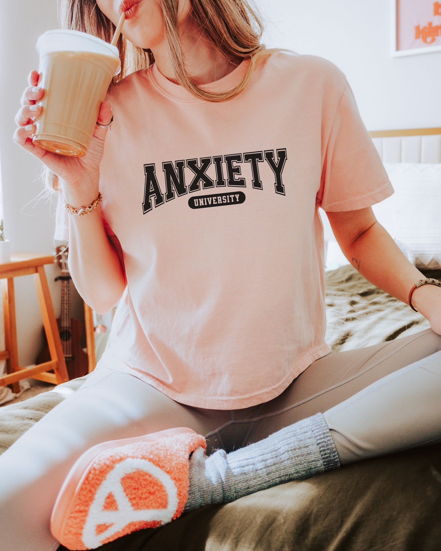 Person wearing a pink t-shirt with 'ANXIETY UNIVERSITY' text, holding a coffee cup.