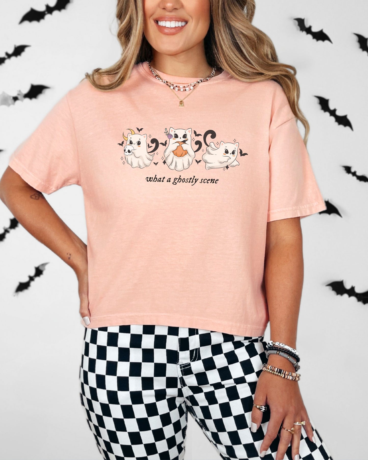 Person wearing a pink t-shirt with cartoon cats and checkered pants on a white background with black bats.