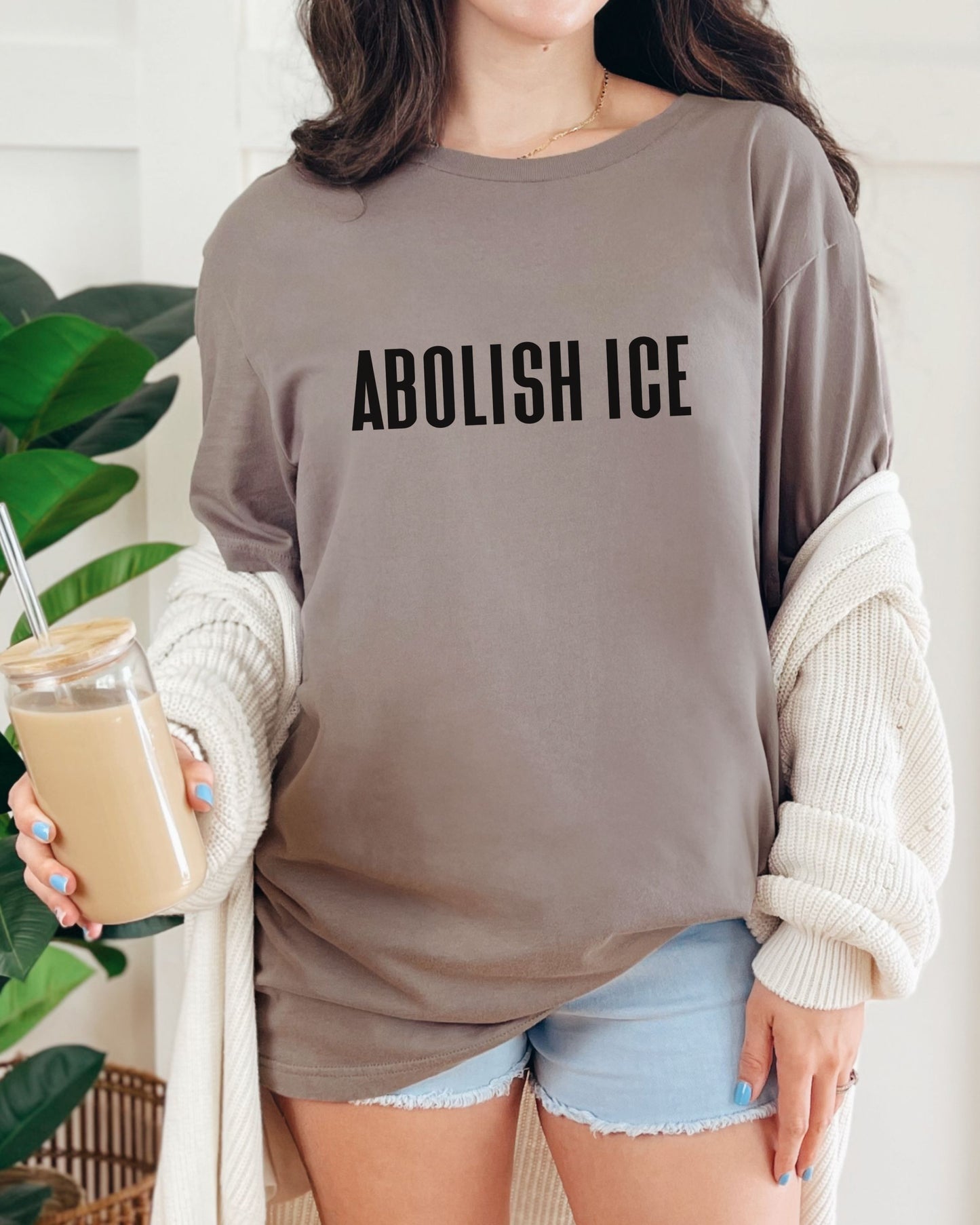 Person wearing a brown sweatshirt with 'ABOLISH ICE' text, holding a drink.