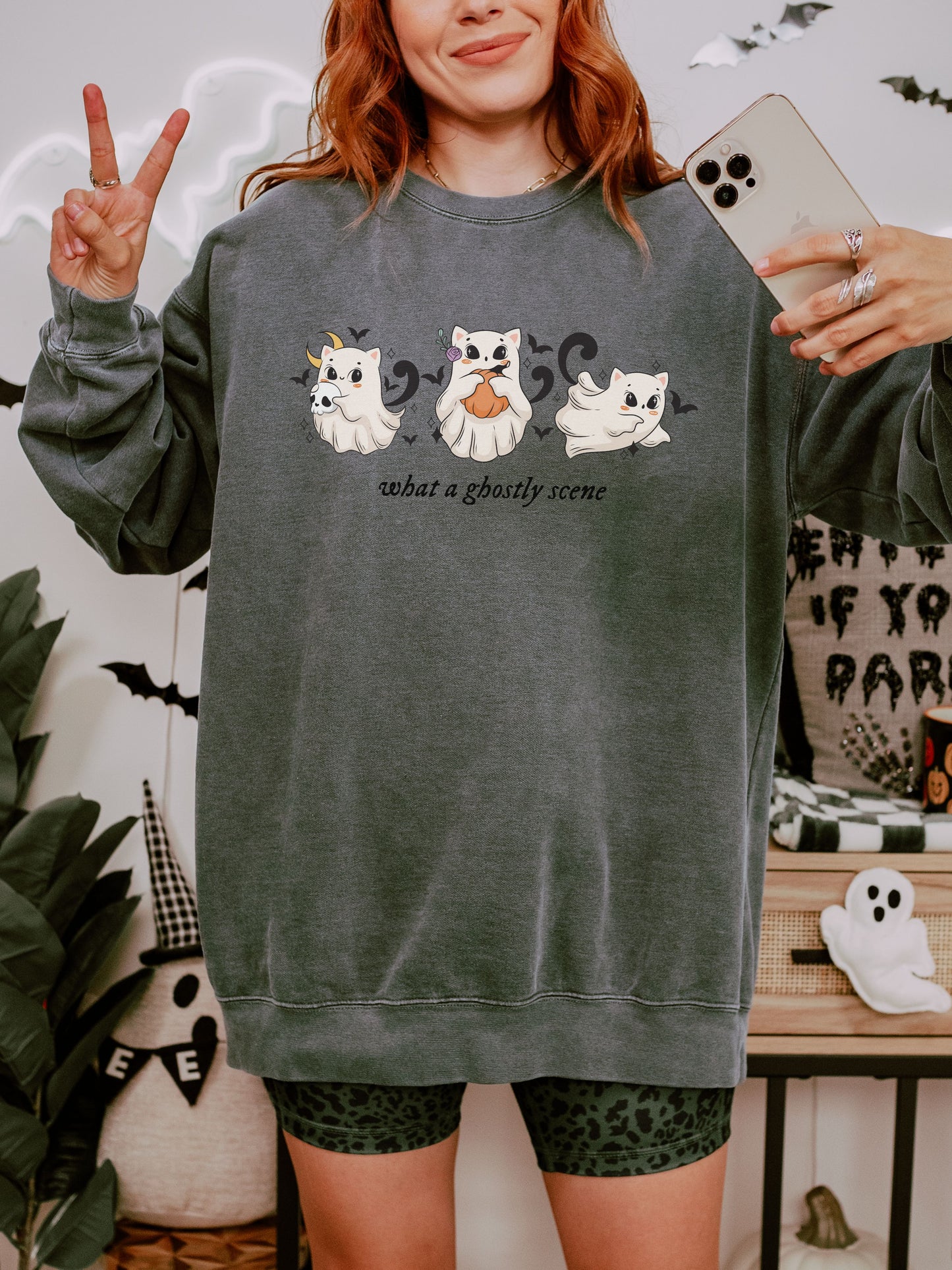 Person wearing a dark green sweatshirt with ghost designs and text, taking a selfie.