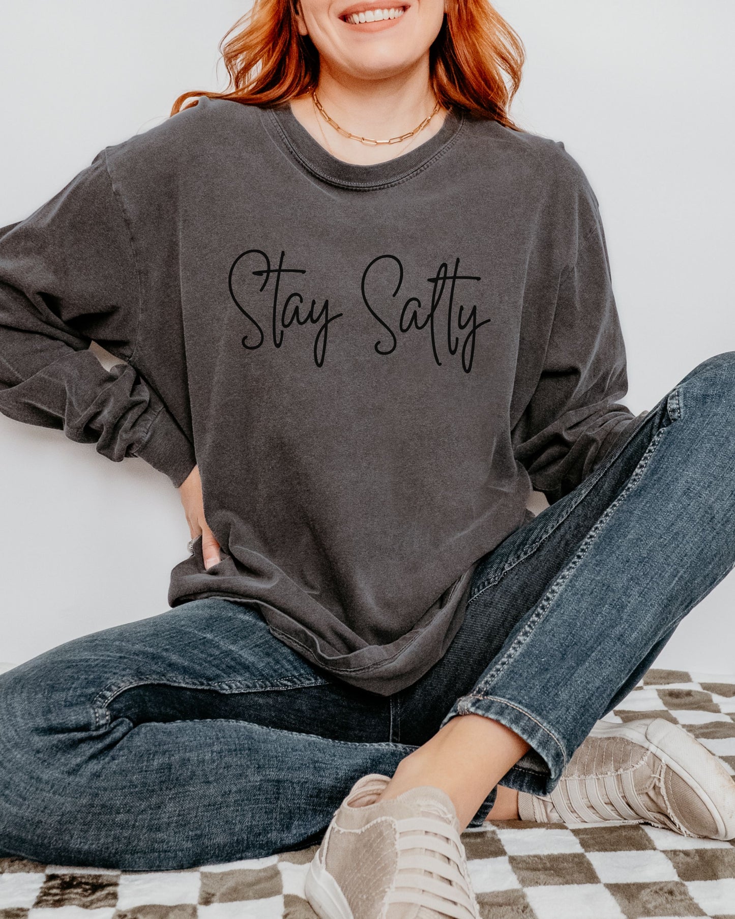 Person wearing a dark gray sweatshirt with 'Stay Salty' text, sitting on a checkered blanket.