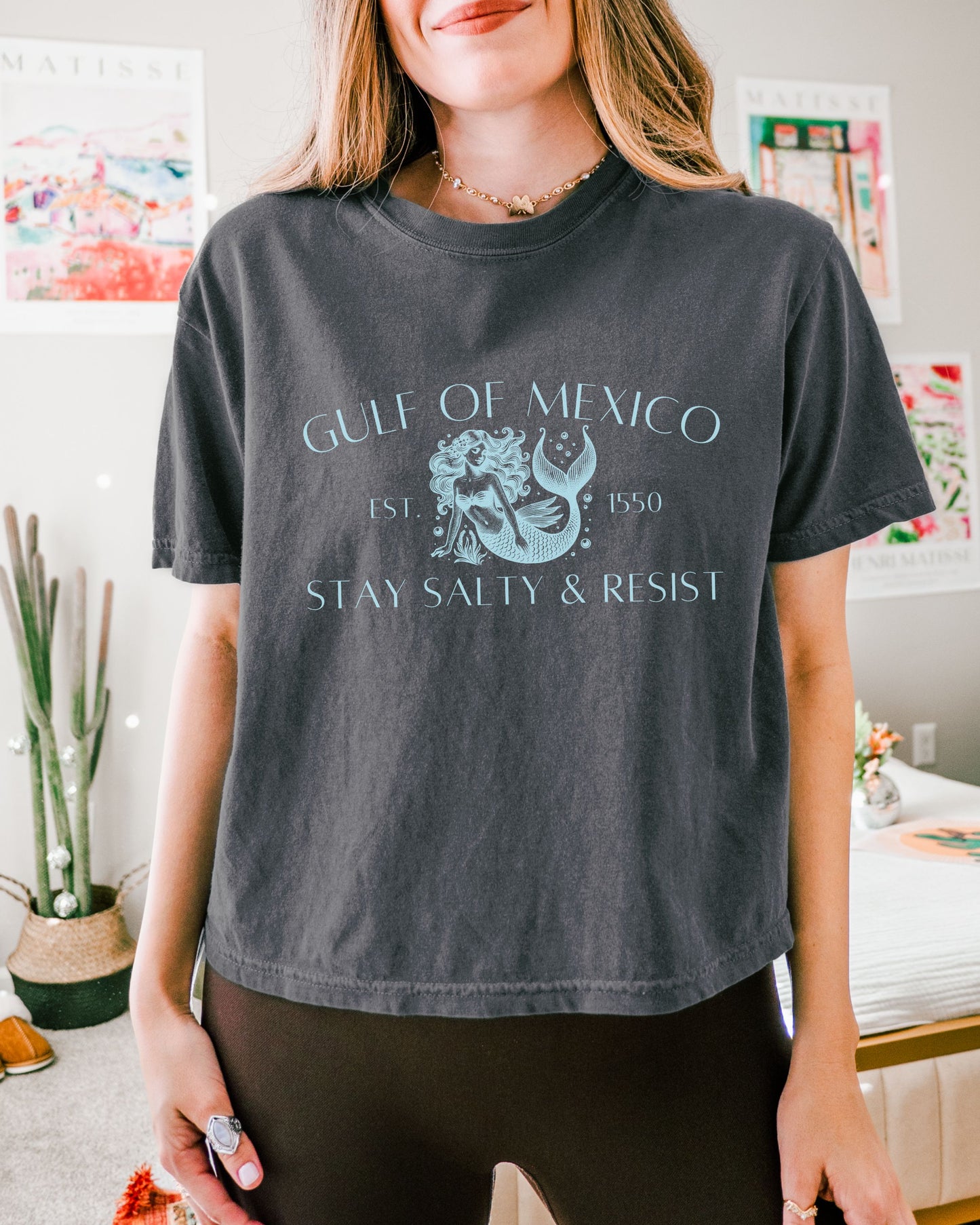 Person wearing a dark gray t-shirt with 'Gulf of Mexico' text and graphic, standing in a casual indoor setting.