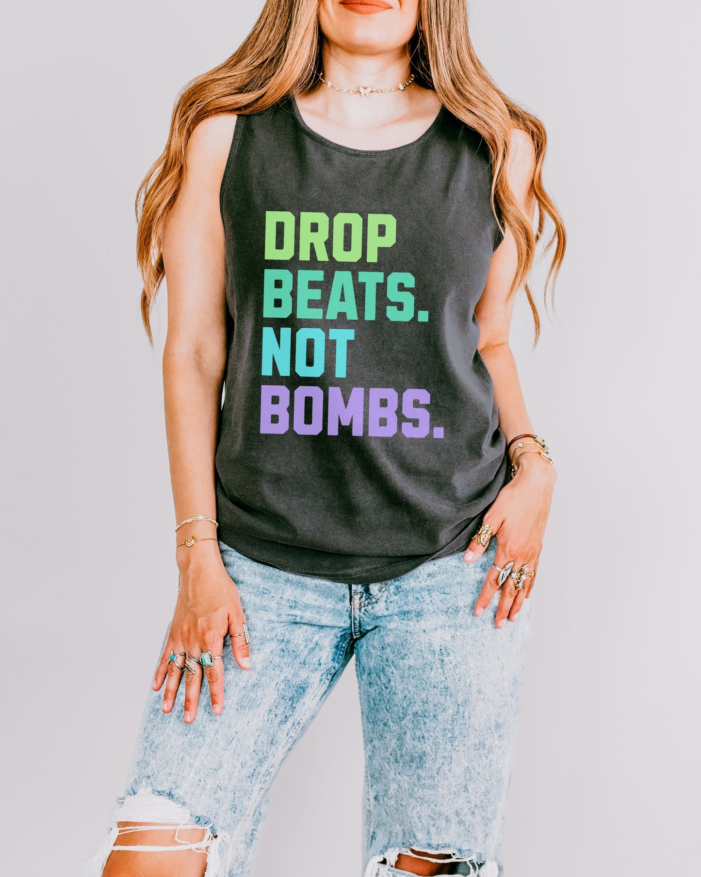 Person wearing a black tank top with colorful text 'DROP BEATS. NOT BOMBS.' on a plain background