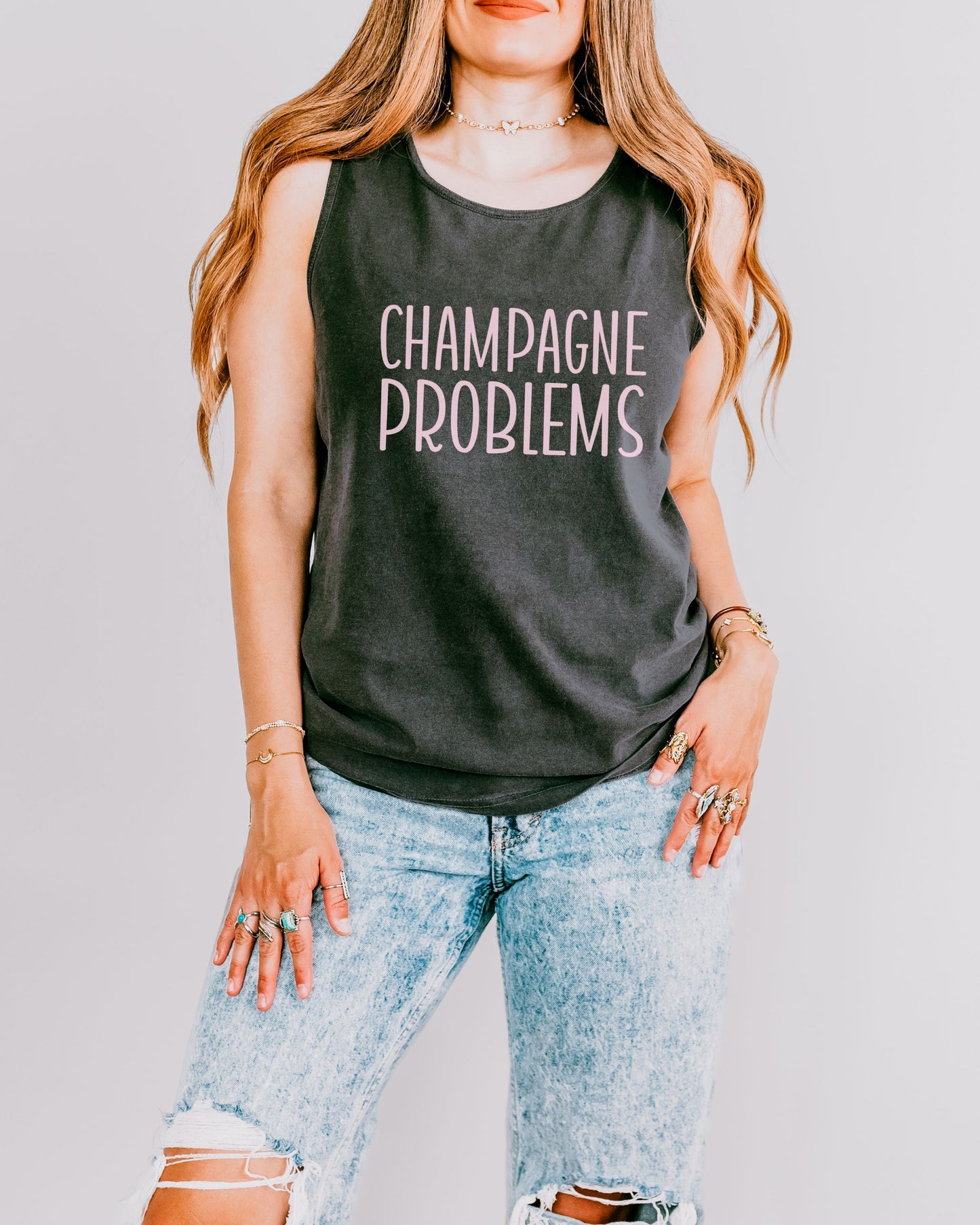Person wearing a dark gray tank top with 'Champagne Problems' text on a plain background