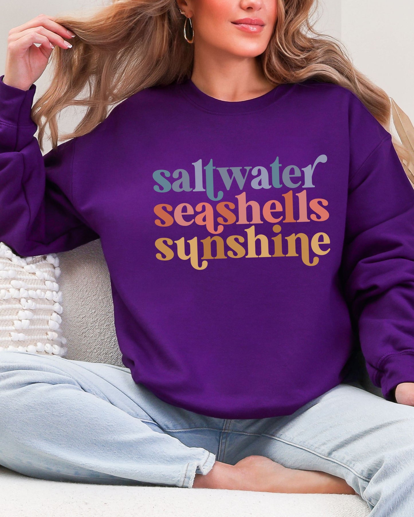 Person wearing a purple sweatshirt with 'saltwater seashells sunshine' text.