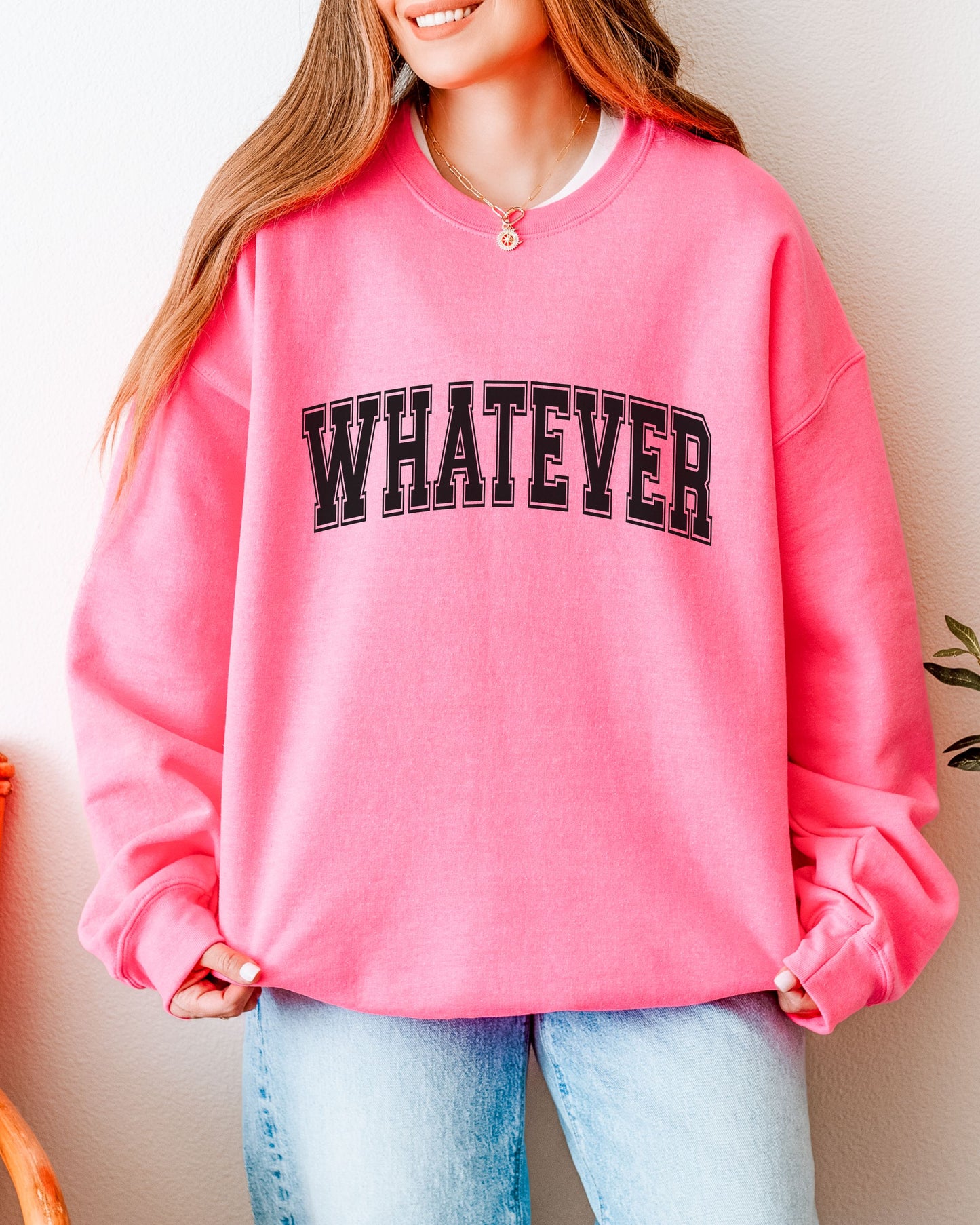 Person wearing a pink sweatshirt with 'WHATEVER' text, standing against a neutral background.