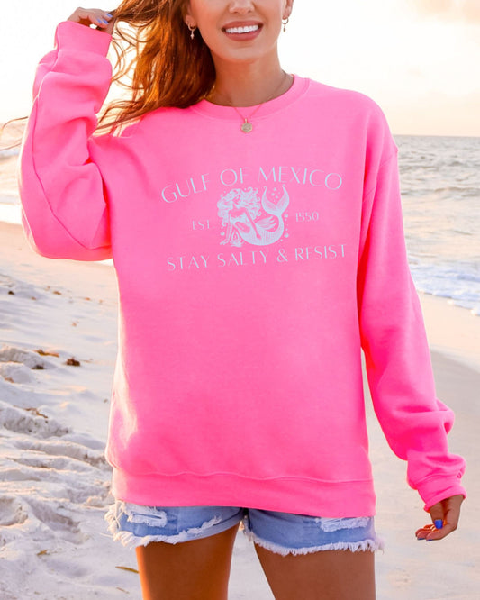 Person wearing a pink sweatshirt with text and graphics on a beach