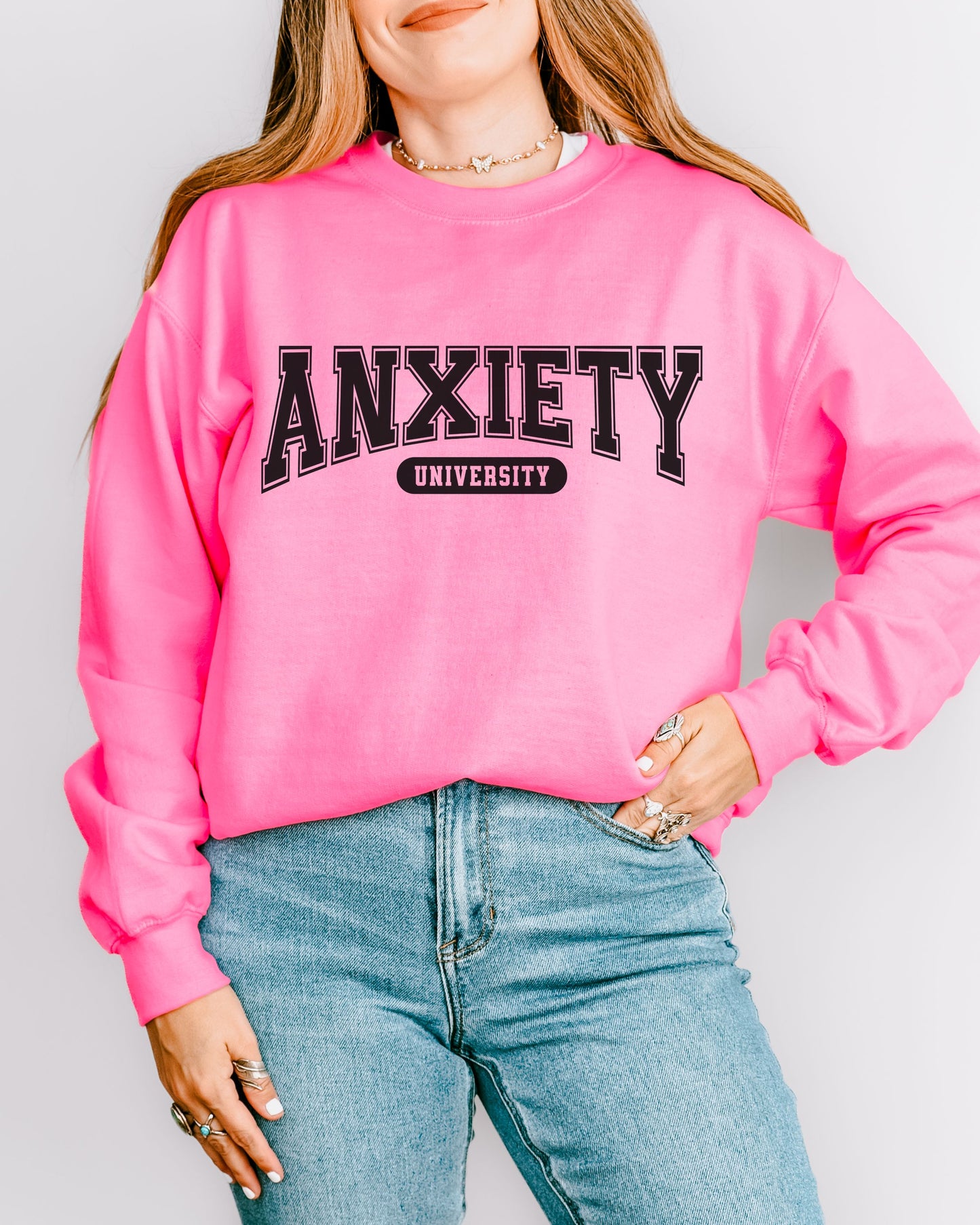 Person wearing a pink sweatshirt with 'ANXIETY UNIVERSITY' text on a plain background