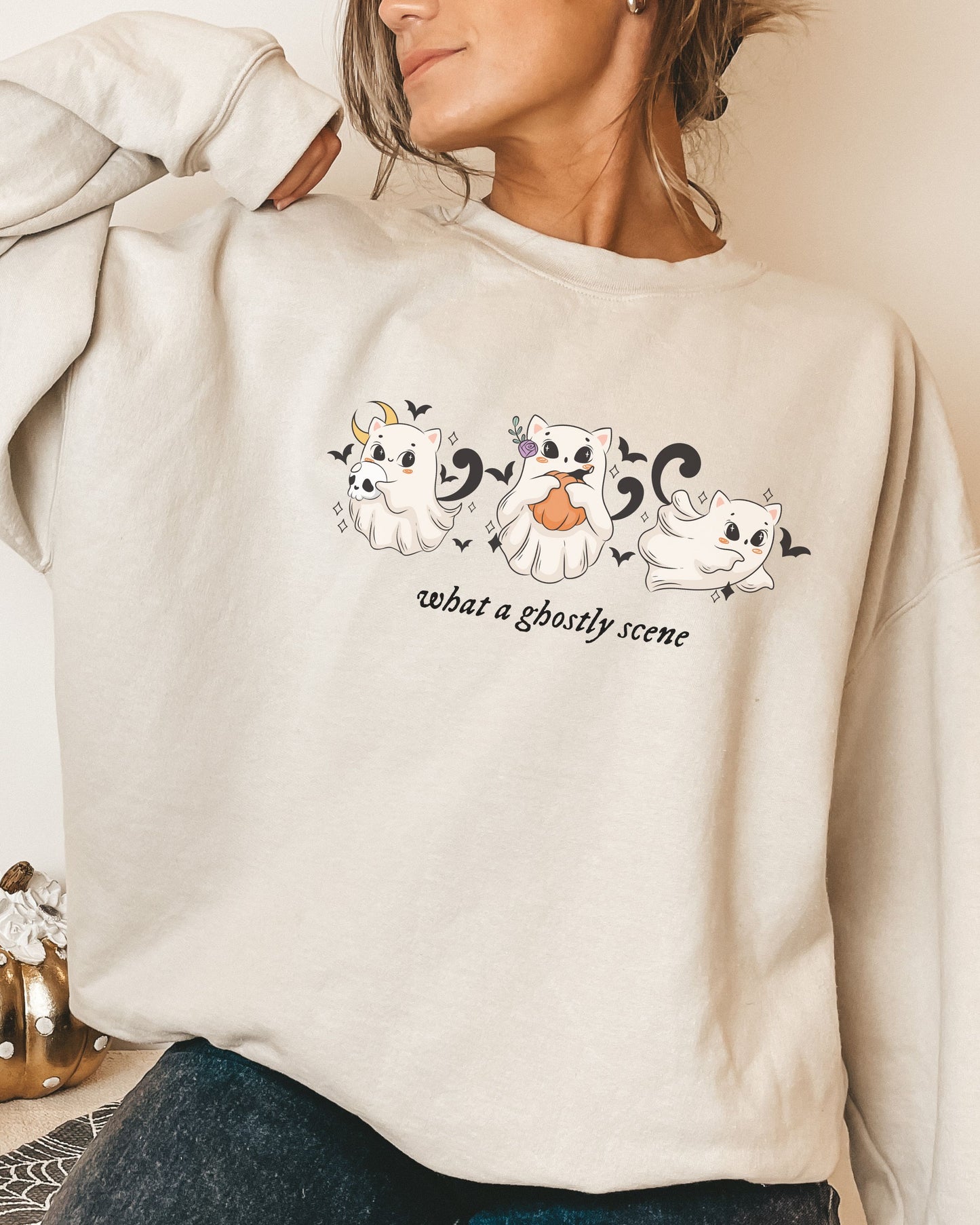 Beige sweatshirt with ghost illustrations and text worn by a person