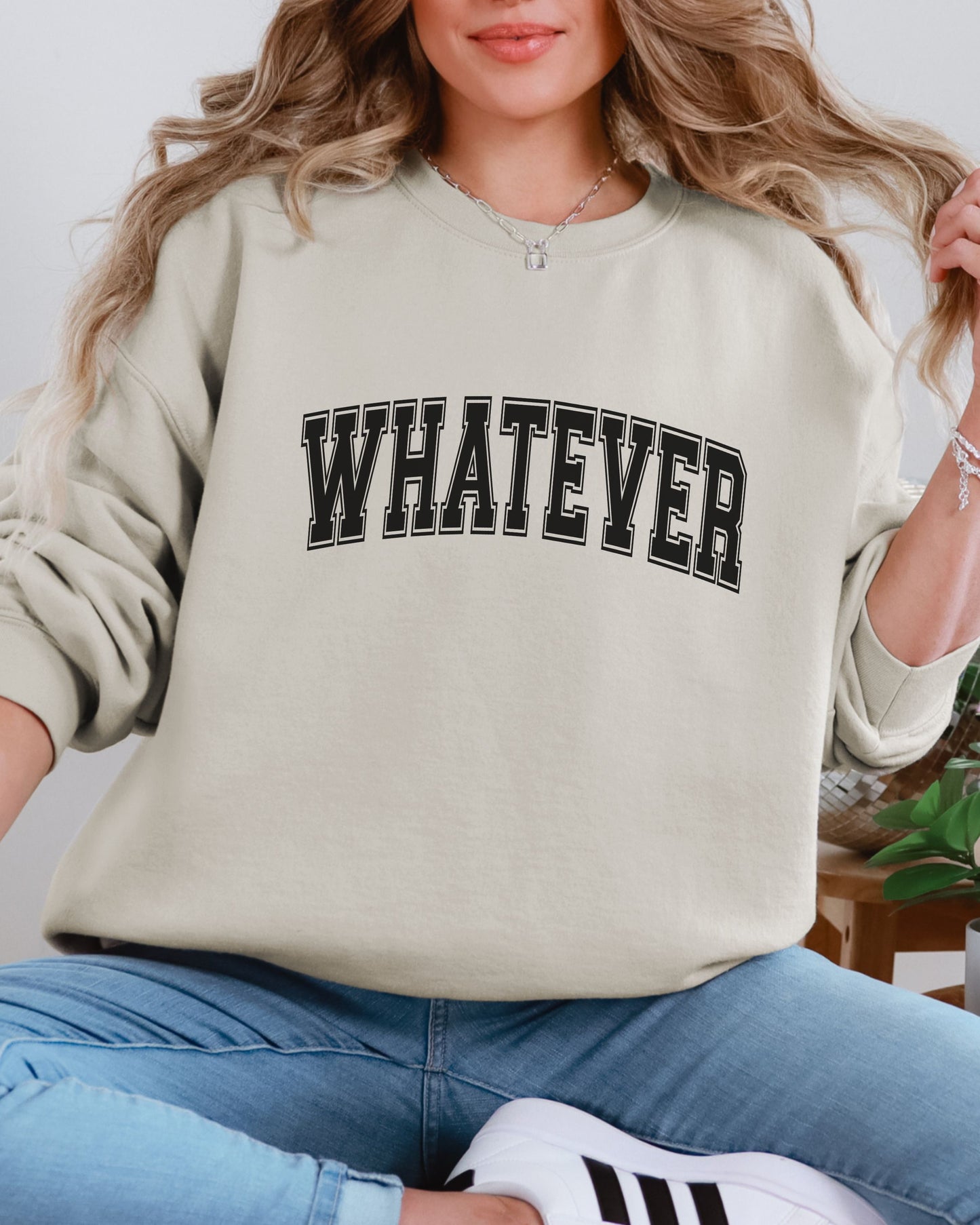 Person wearing a beige sweatshirt with 'WHATEVER' text, sitting on a white background