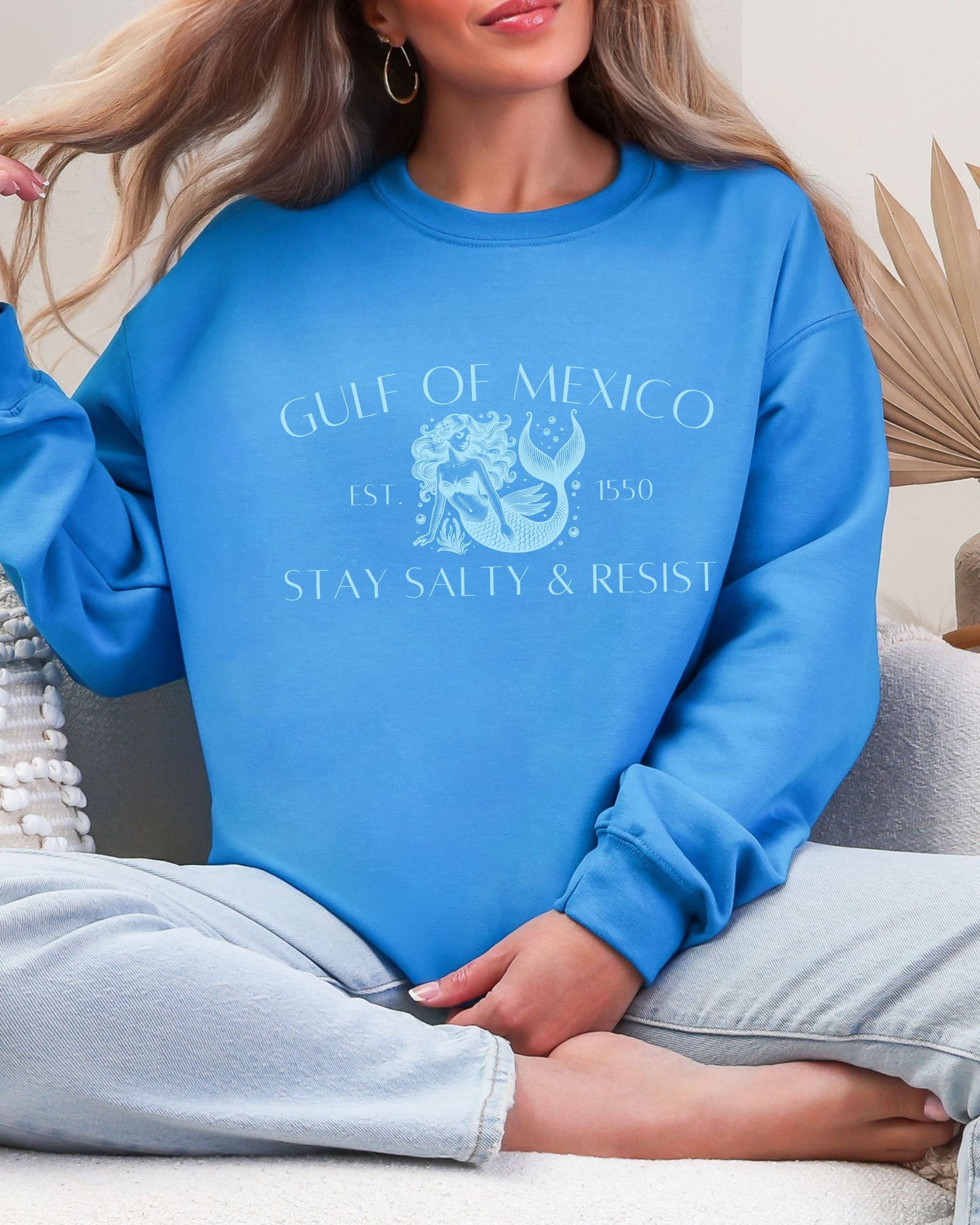 Person wearing a blue sweatshirt with text and graphics, sitting on a couch.
