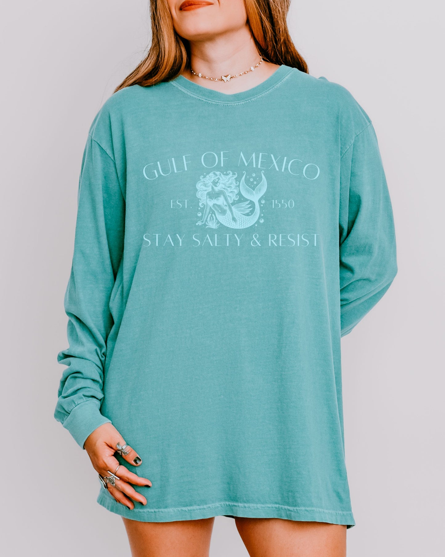 Person wearing a teal long-sleeve shirt with a graphic design on a plain background
