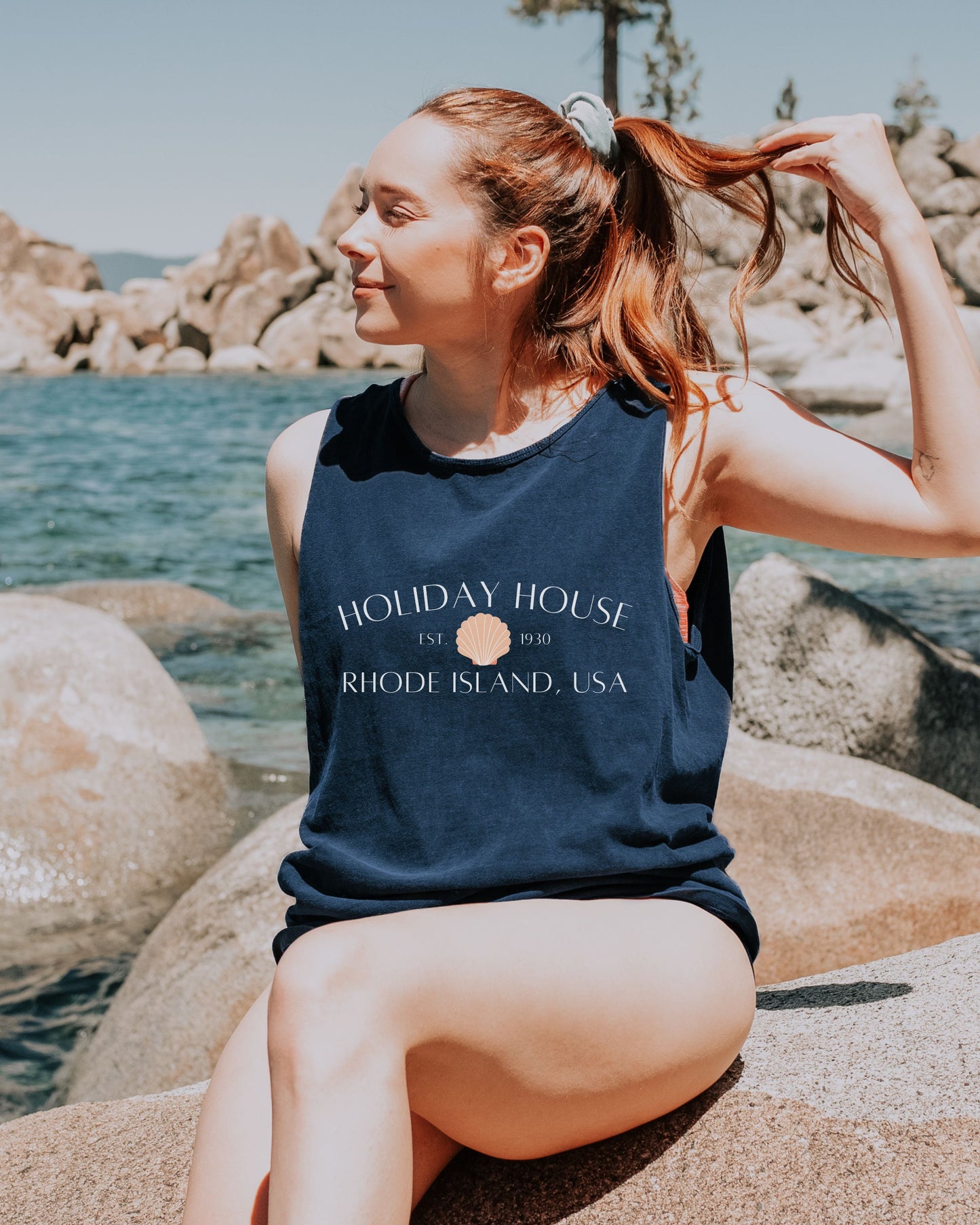 Woman sitting by a body of water wearing a navy blue tank top with text.